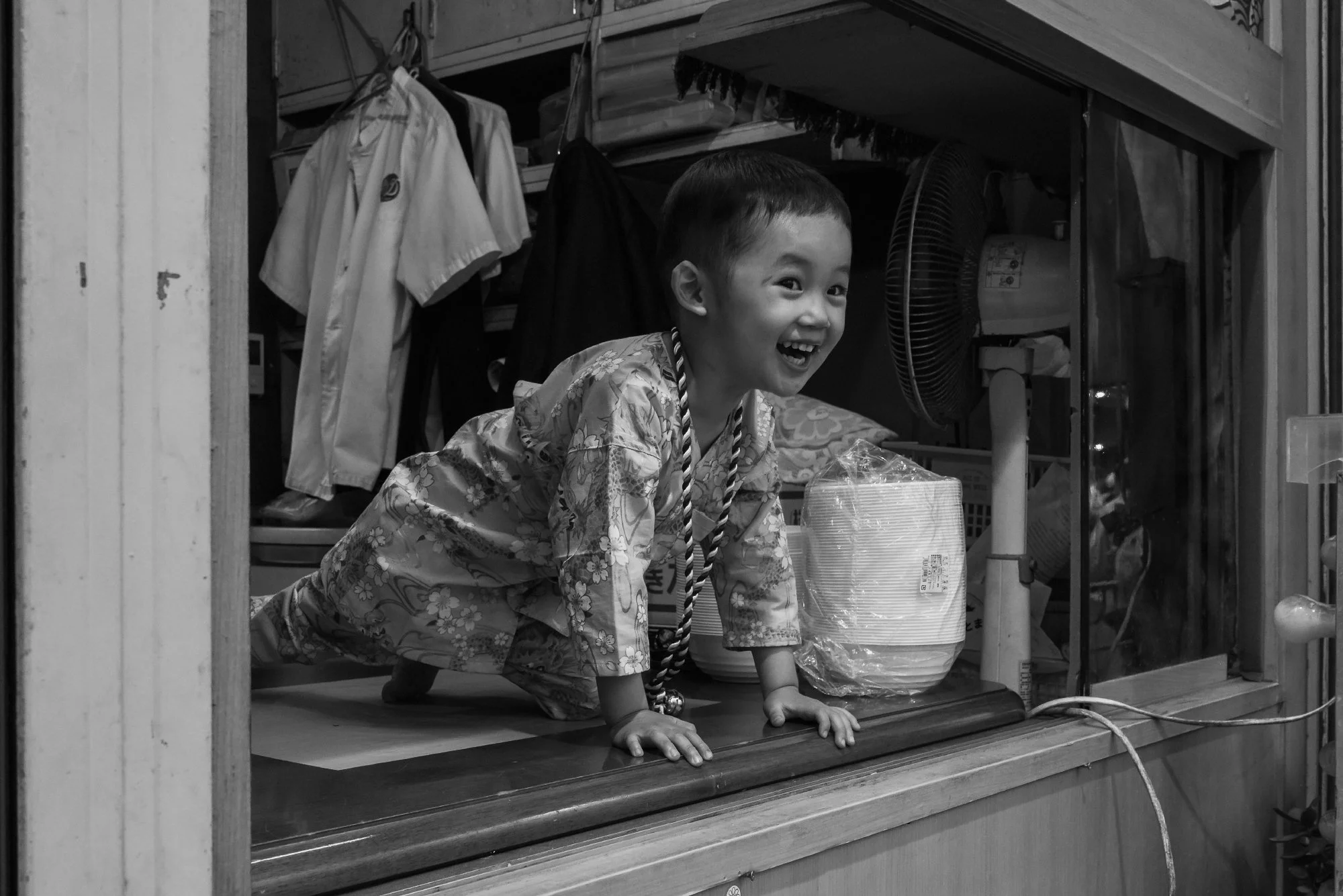 Print AD-0028. A smiling child leaning through an open shop window.