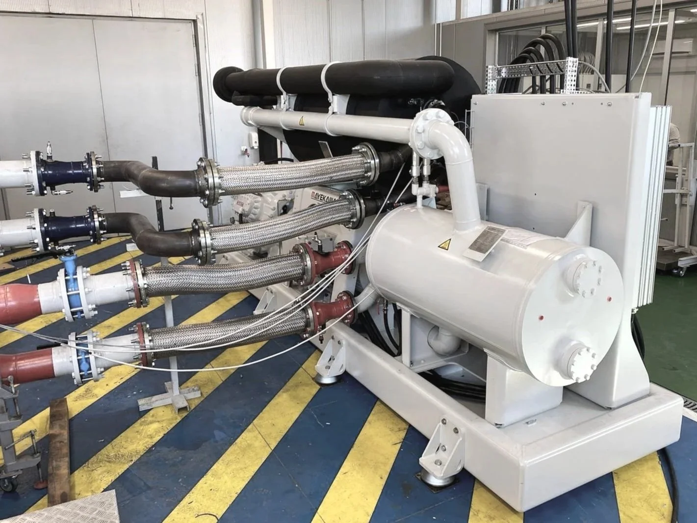 Industrial machine with multiple pipes and hoses in a factory or lab setting.