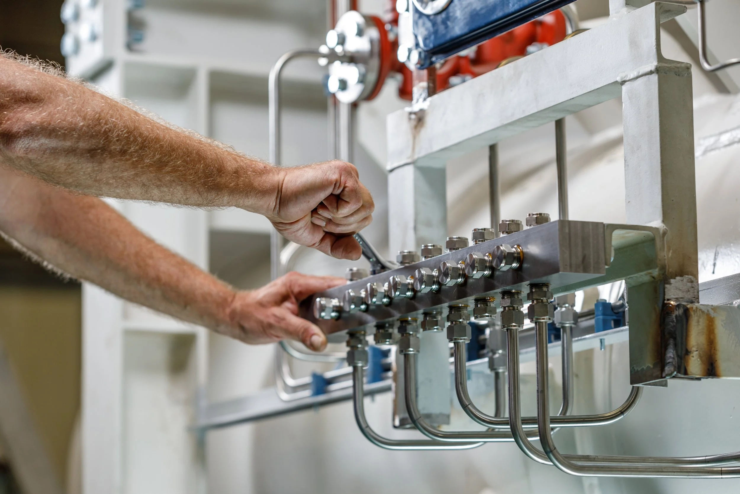 A person using a wrench to adjust or tighten a component of a mechanical system with multiple pipes and fittings.