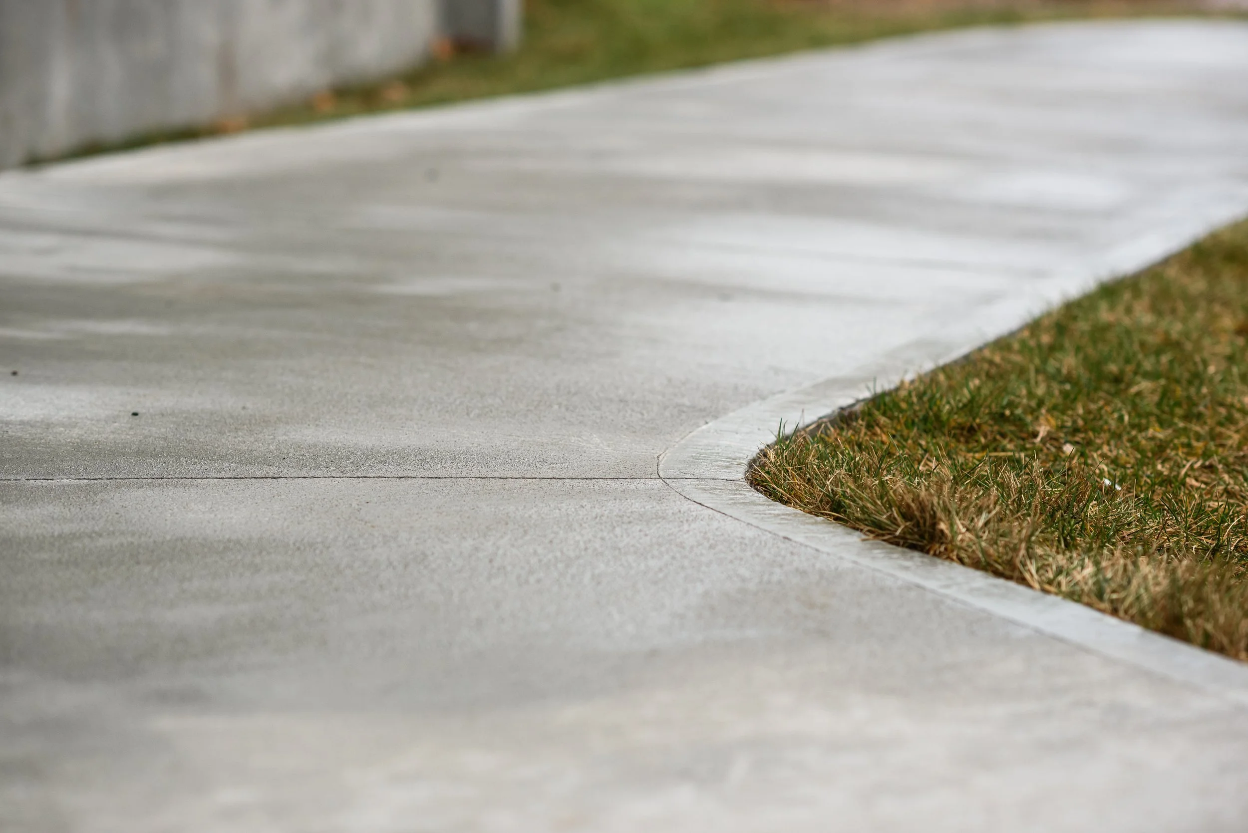Close-up of a curved concrete sidewalk with grass on the side.