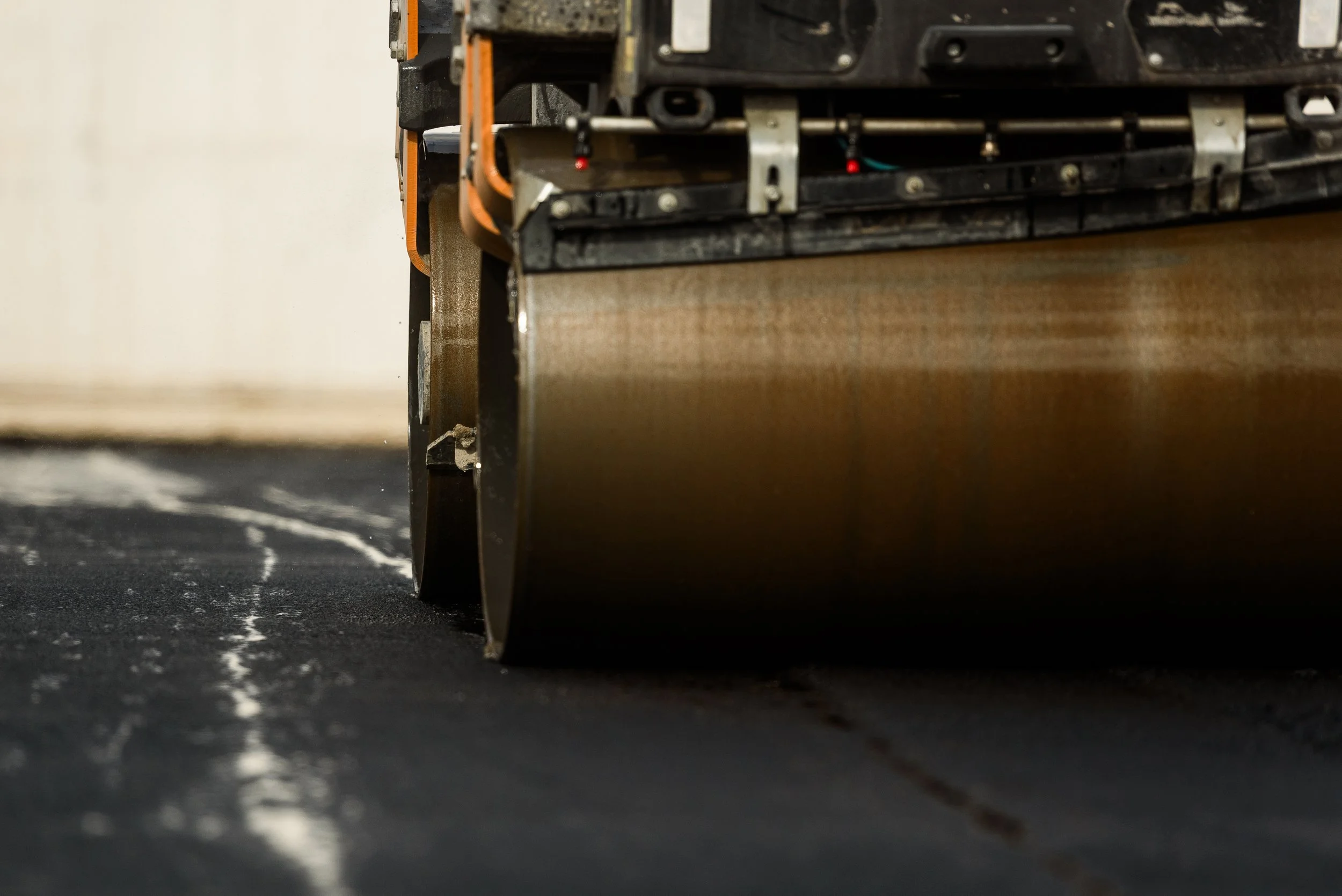 Close-up of a robotic floor sweeper cleaning a black textured floor, showing its cylindrical brush and part of its black and orange body.