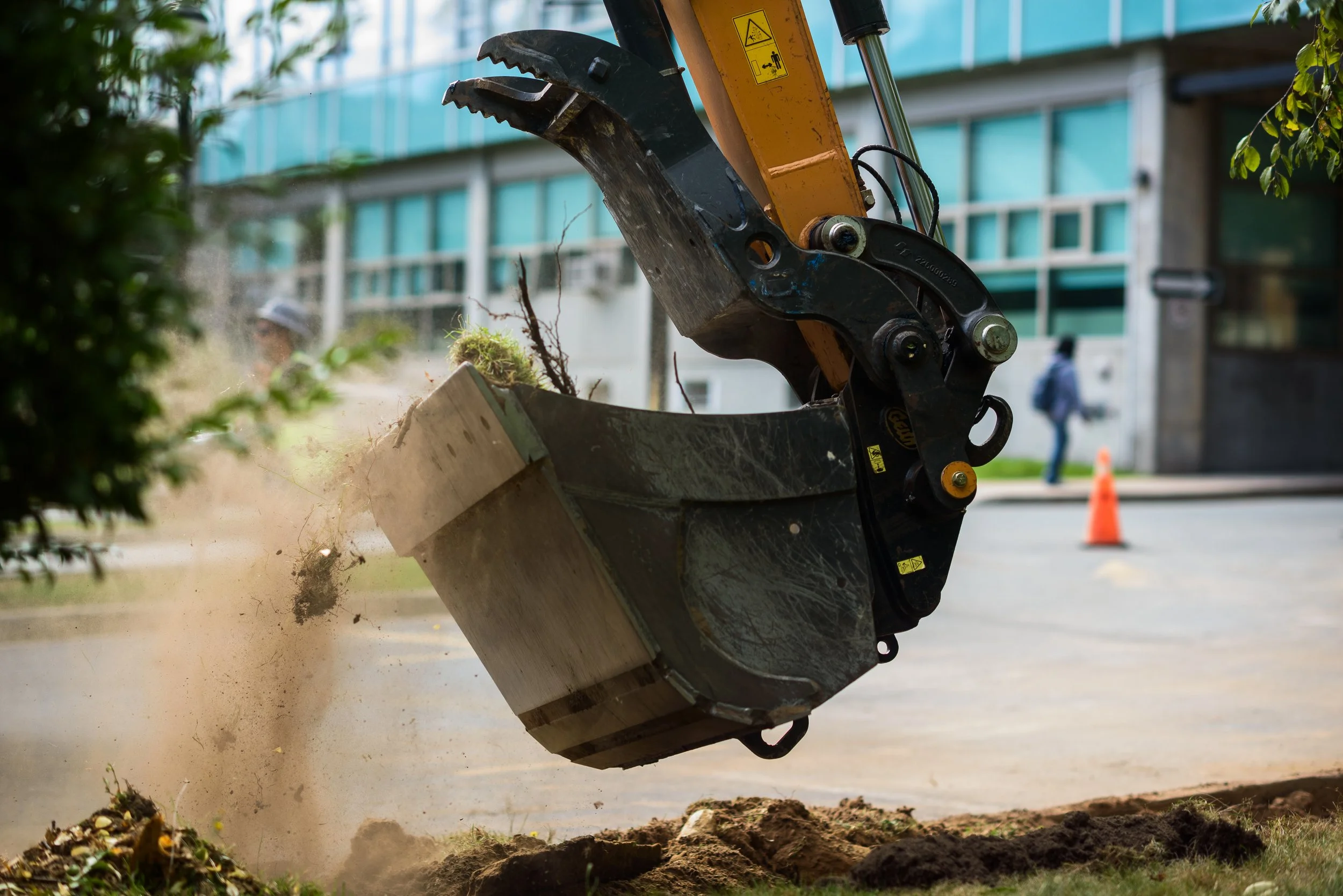 Close-up of a construction excavator bucket digging into the ground, with dust and soil flying.