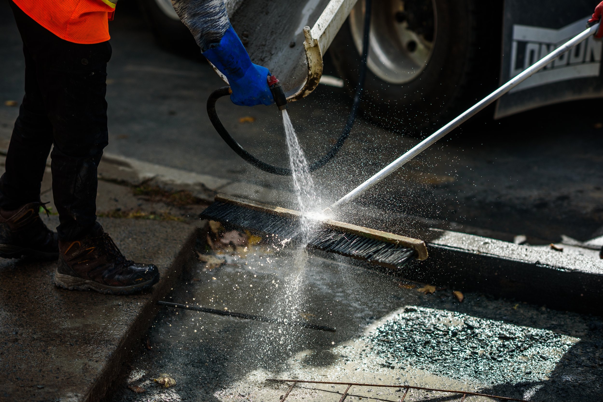 Worker in safety gear power washing a street.