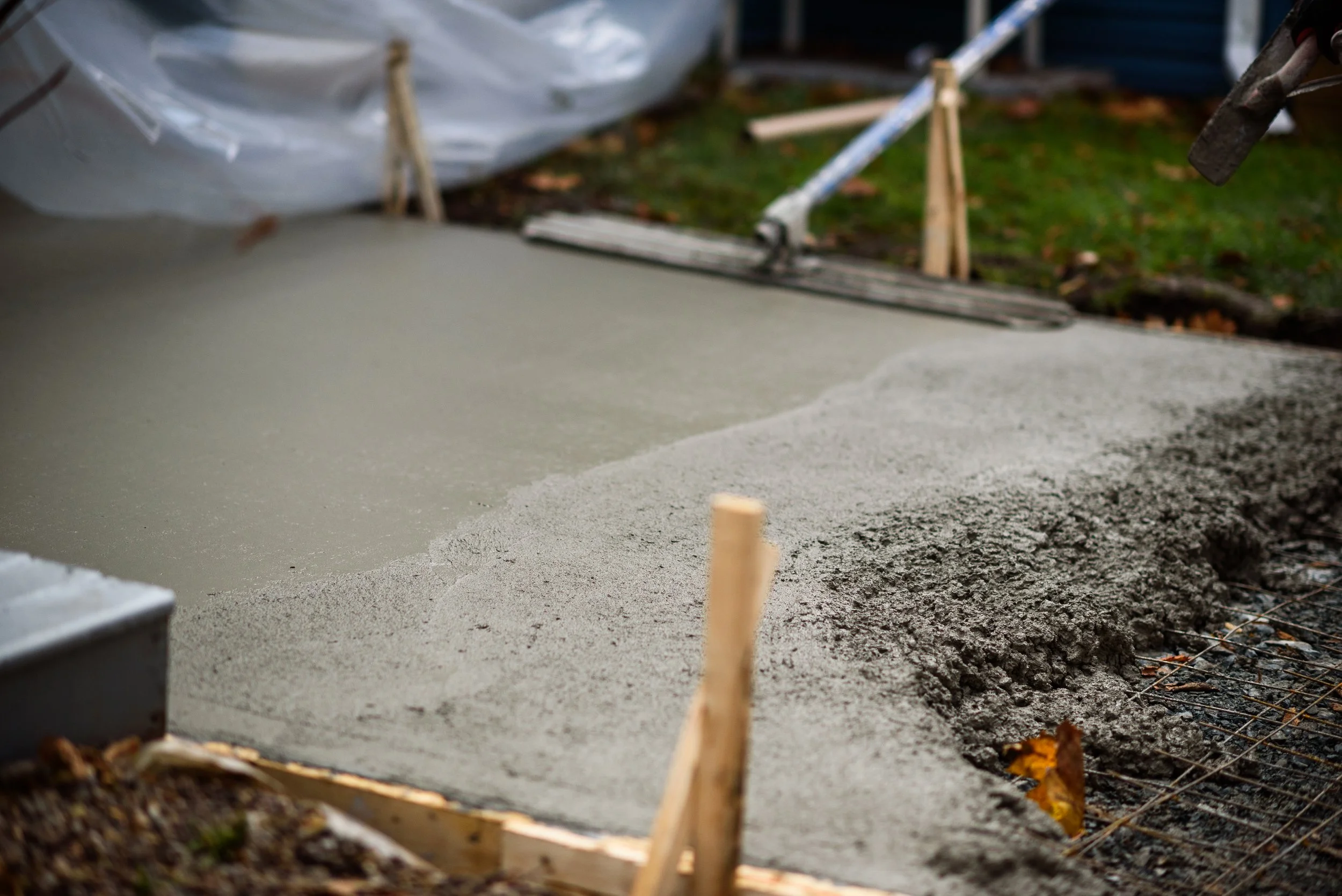 Freshly poured concrete slab on a construction site with wooden and metal supports, surrounded by dirt and construction materials.