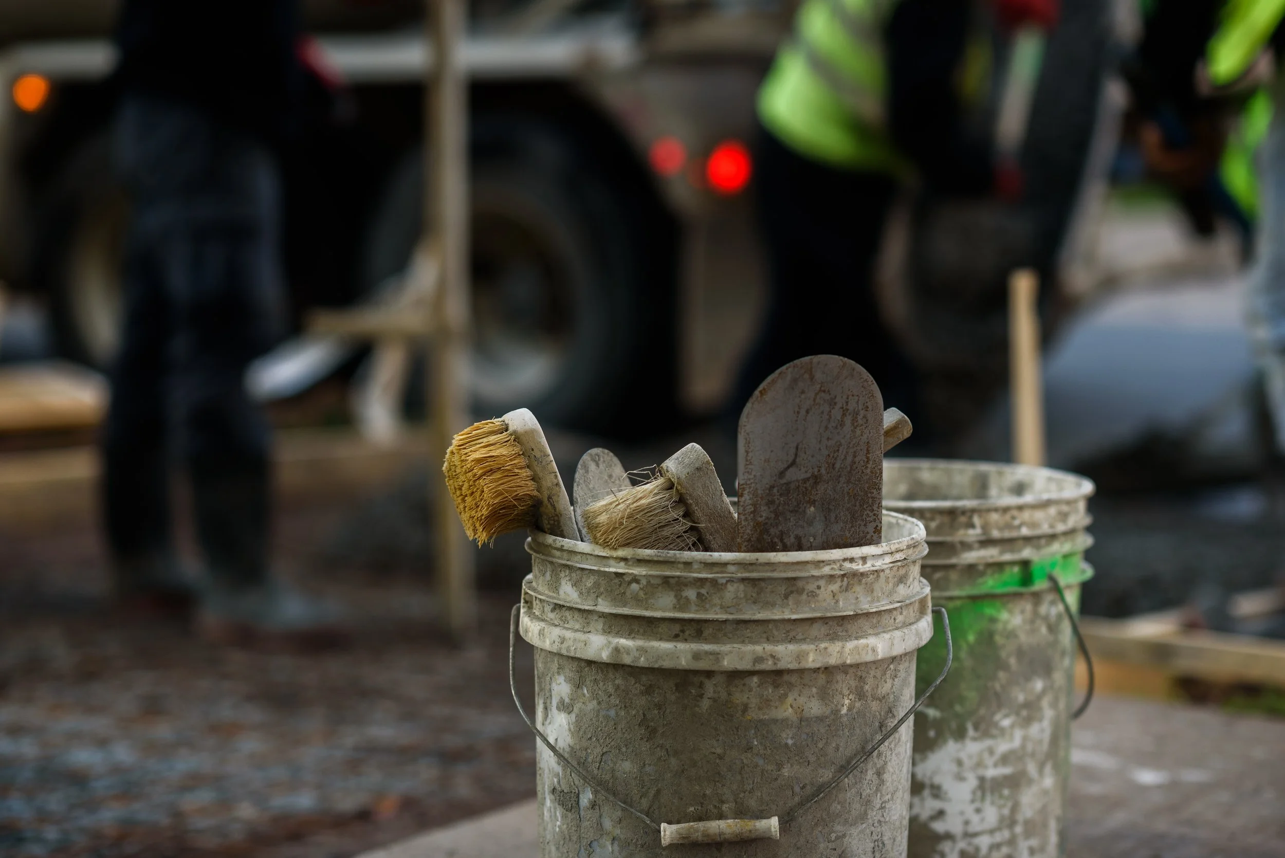 Dirty paint brushes and trowels in a paint bucket on a construction site.