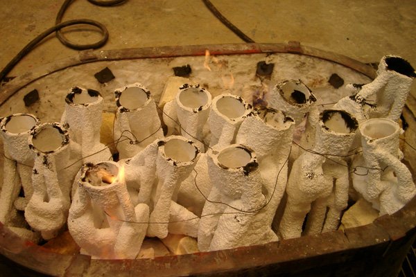 After the wax is burned out, the investments are allowed to cool and then they are re-positioned in the same kiln that was used for the burn out, now with the pour cups facing the ceiling. The tubes at the top of the photo are the flexible gas tubing
