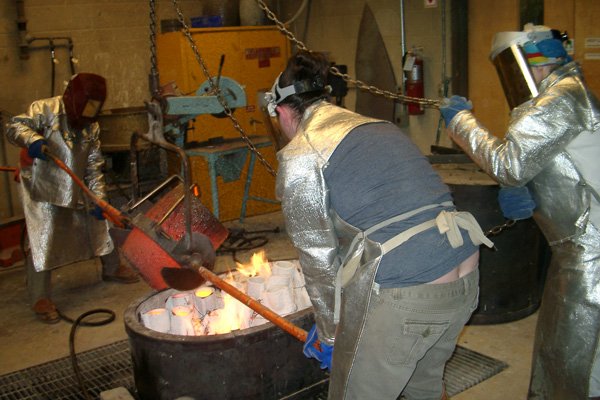 I handle raising and lowering the burn-out kiln top and move the crucible horizontally above the investments. Line pours while Sam moves the crucible every so skillfully over the pour cups.