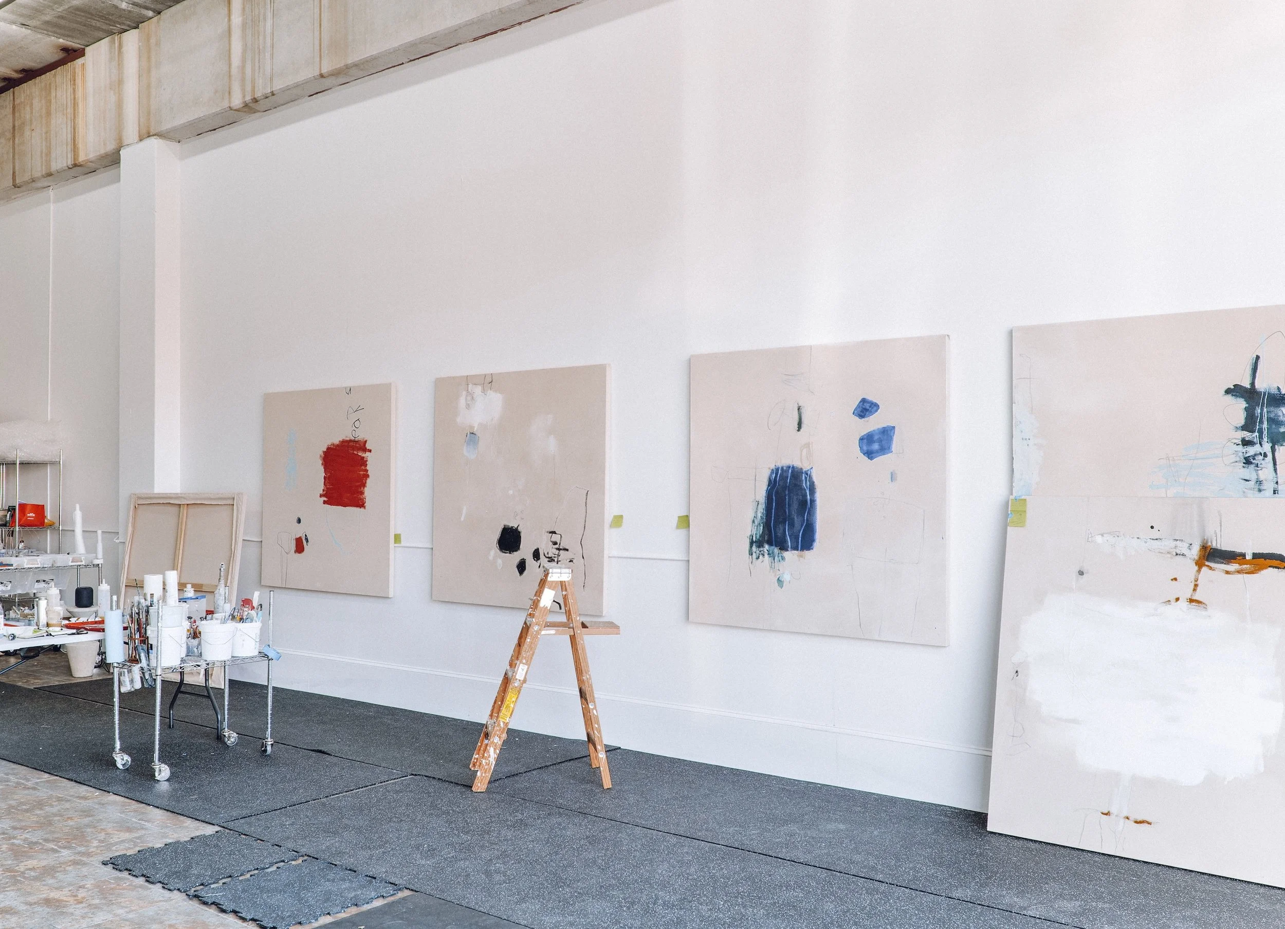 Artist studio with large abstract paintings in progress, natural light, and open space during a reflective creative process