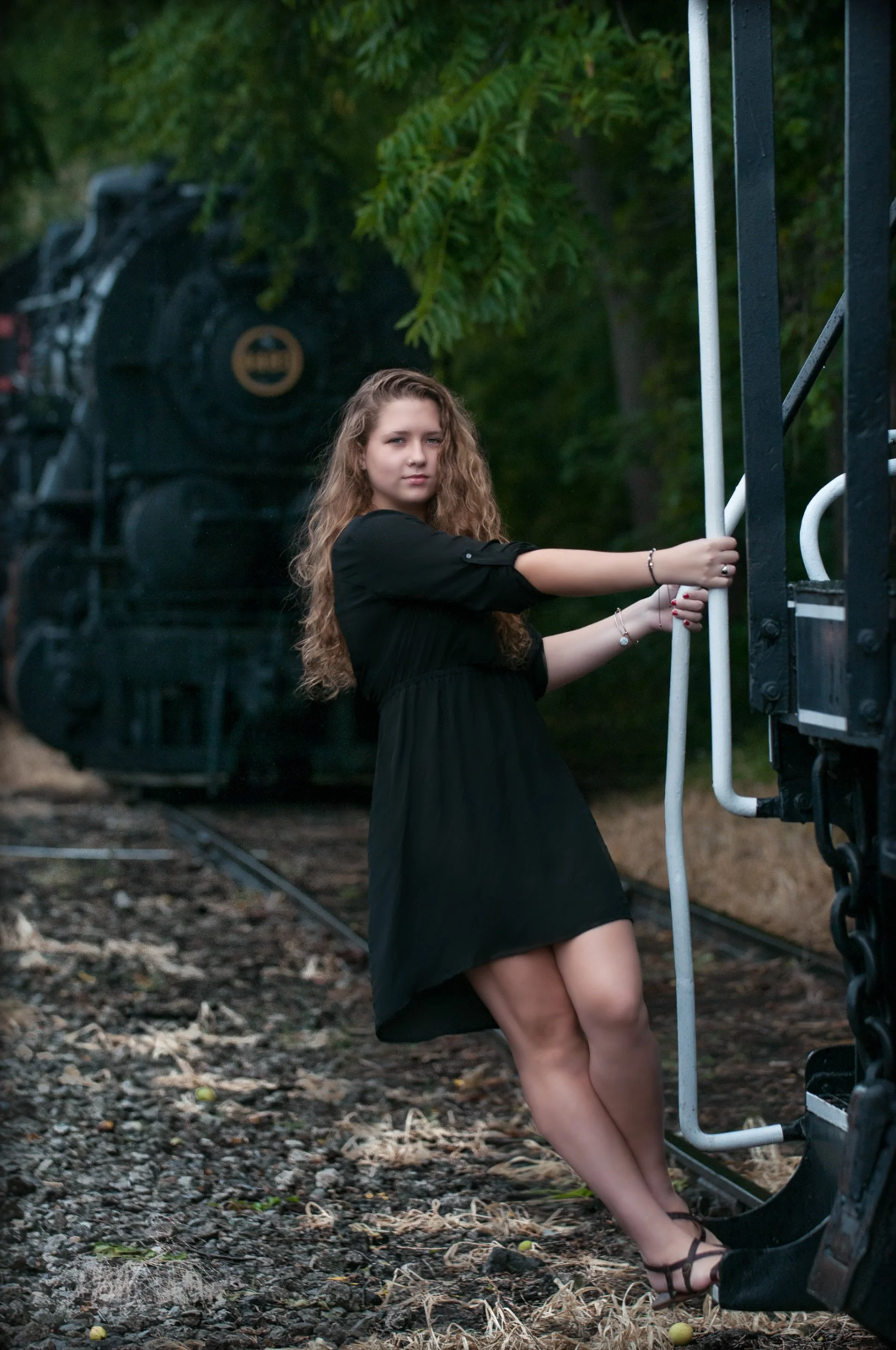 Senior in a black dress holding the laser of a choose with a black steam locomotive behind her.