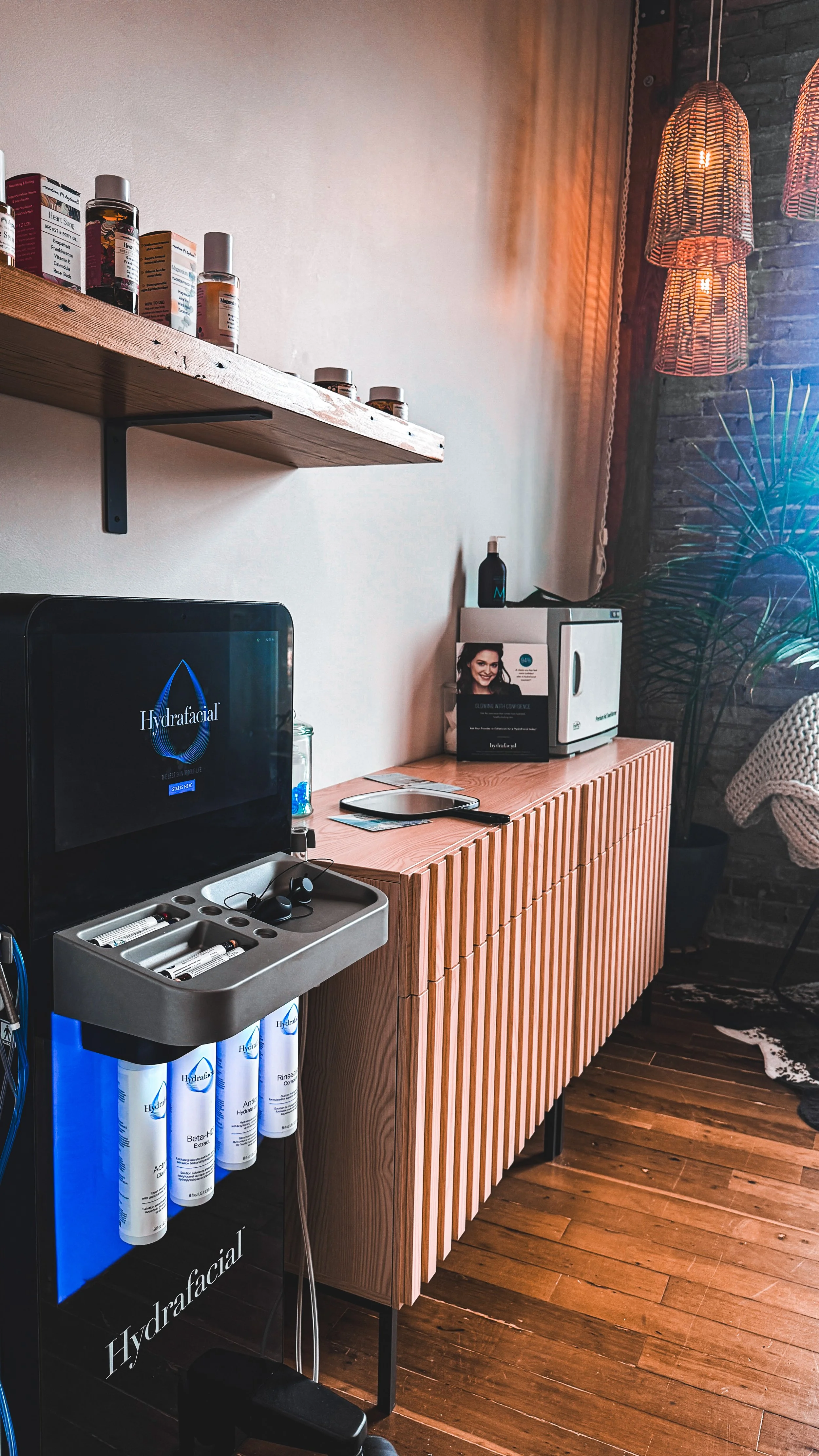 Interior room at outbound wellness center with a hydrafacial machine, products and decorated with hanging pendant lights and a brick wall in the background.