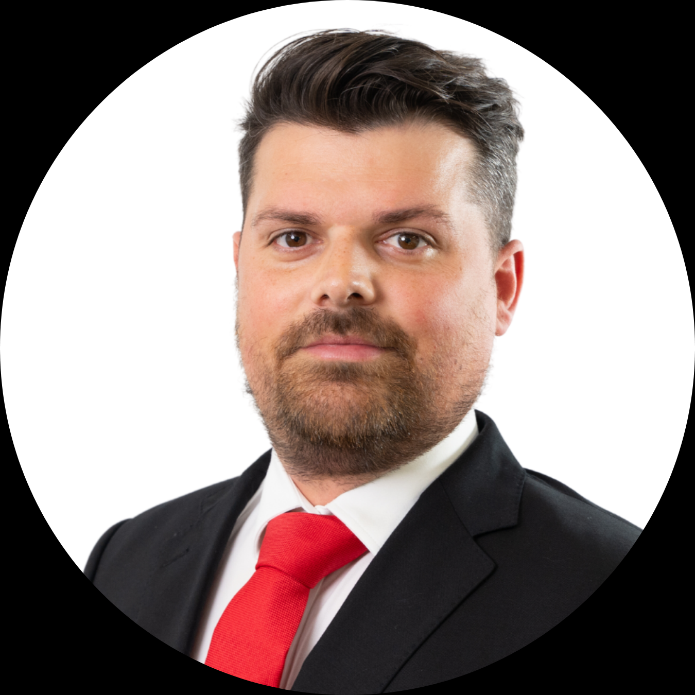 A man in a black suit with a red tie and white shirt, looking directly at the camera against a white background.