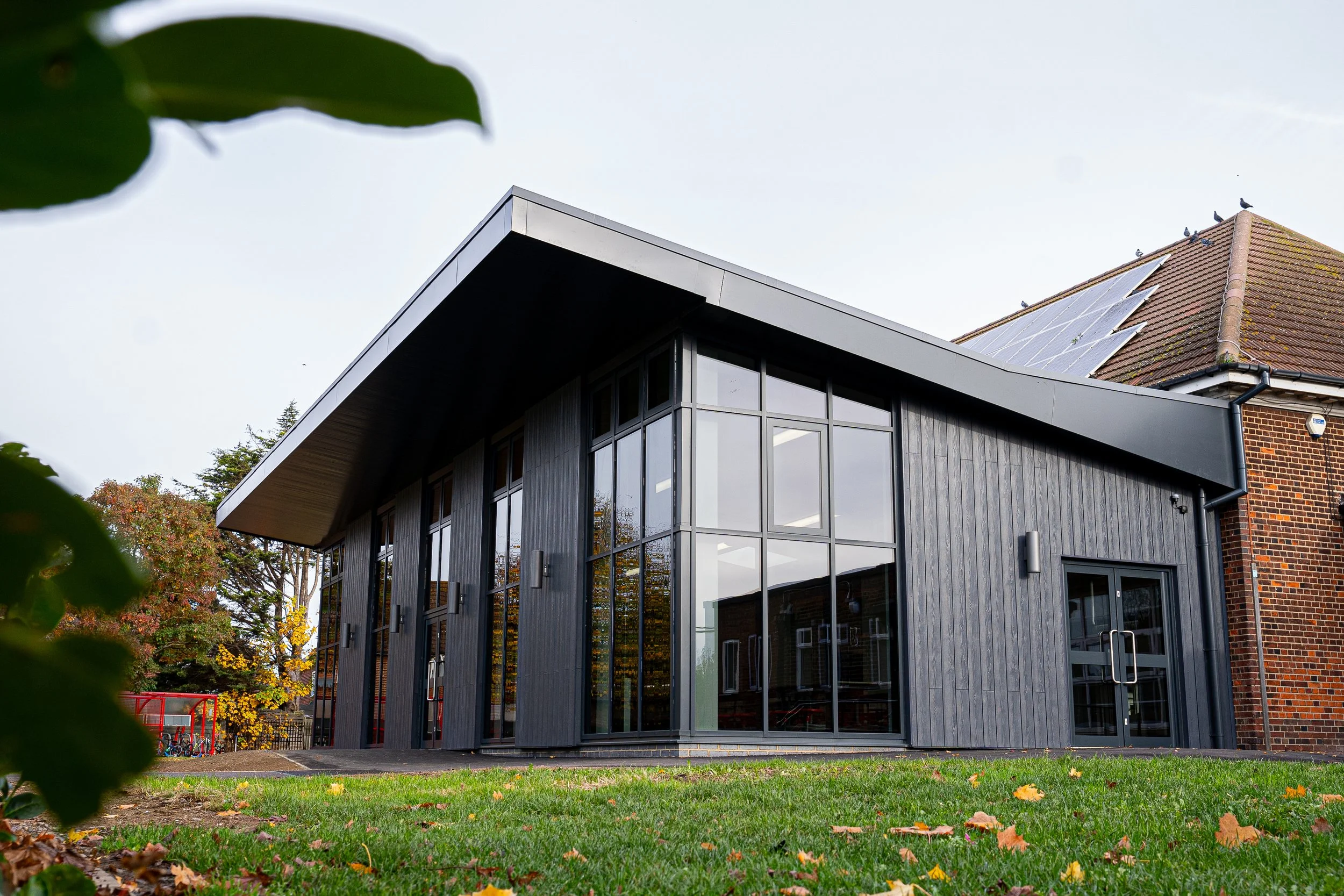 A spacious cafeteria with white tables and red stools, large windows, and double doors leading outside.