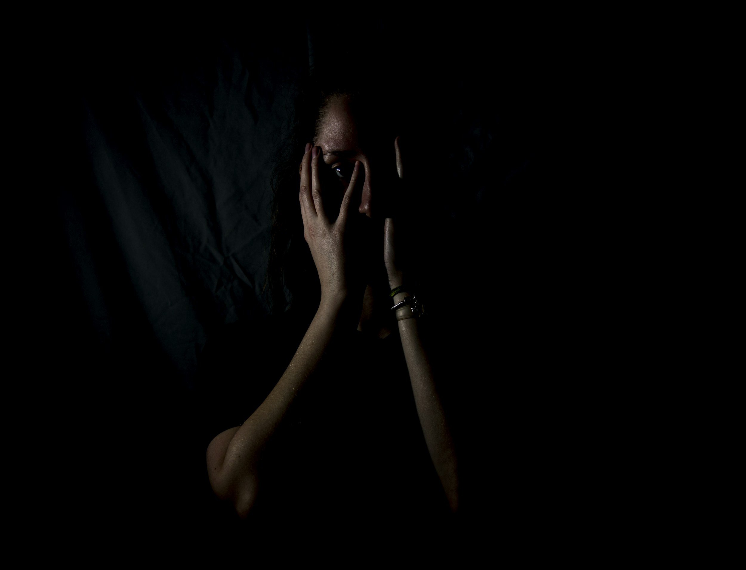 A person in a dark room with hands on their face.