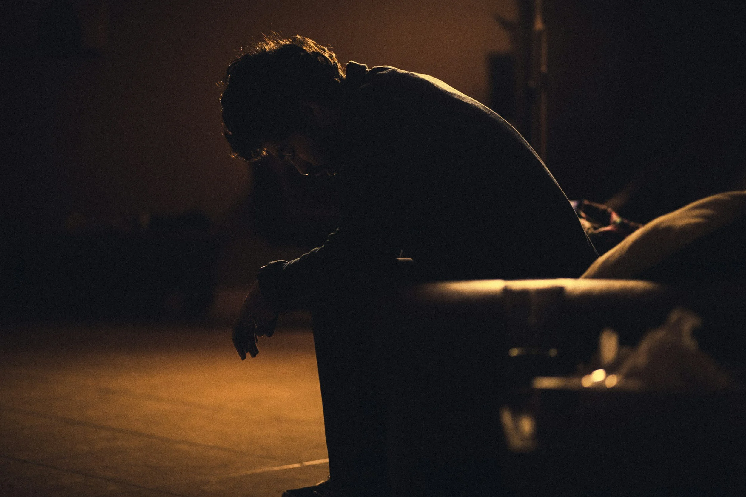Person sitting alone in a dim room with their head lowered, appearing emotionally overwhelmed