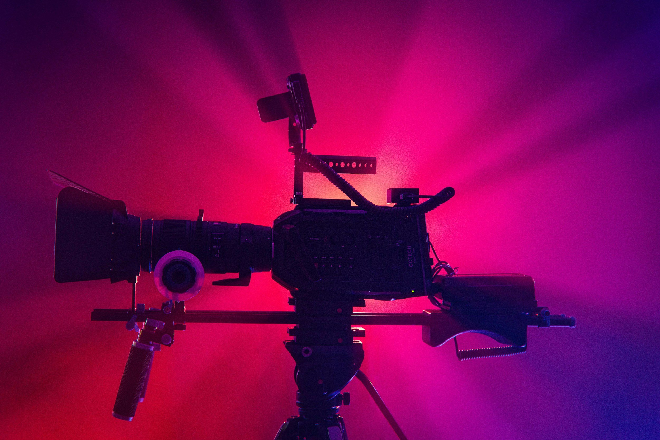 Video camera on a tripod silhouette against a pink and purple foggy background