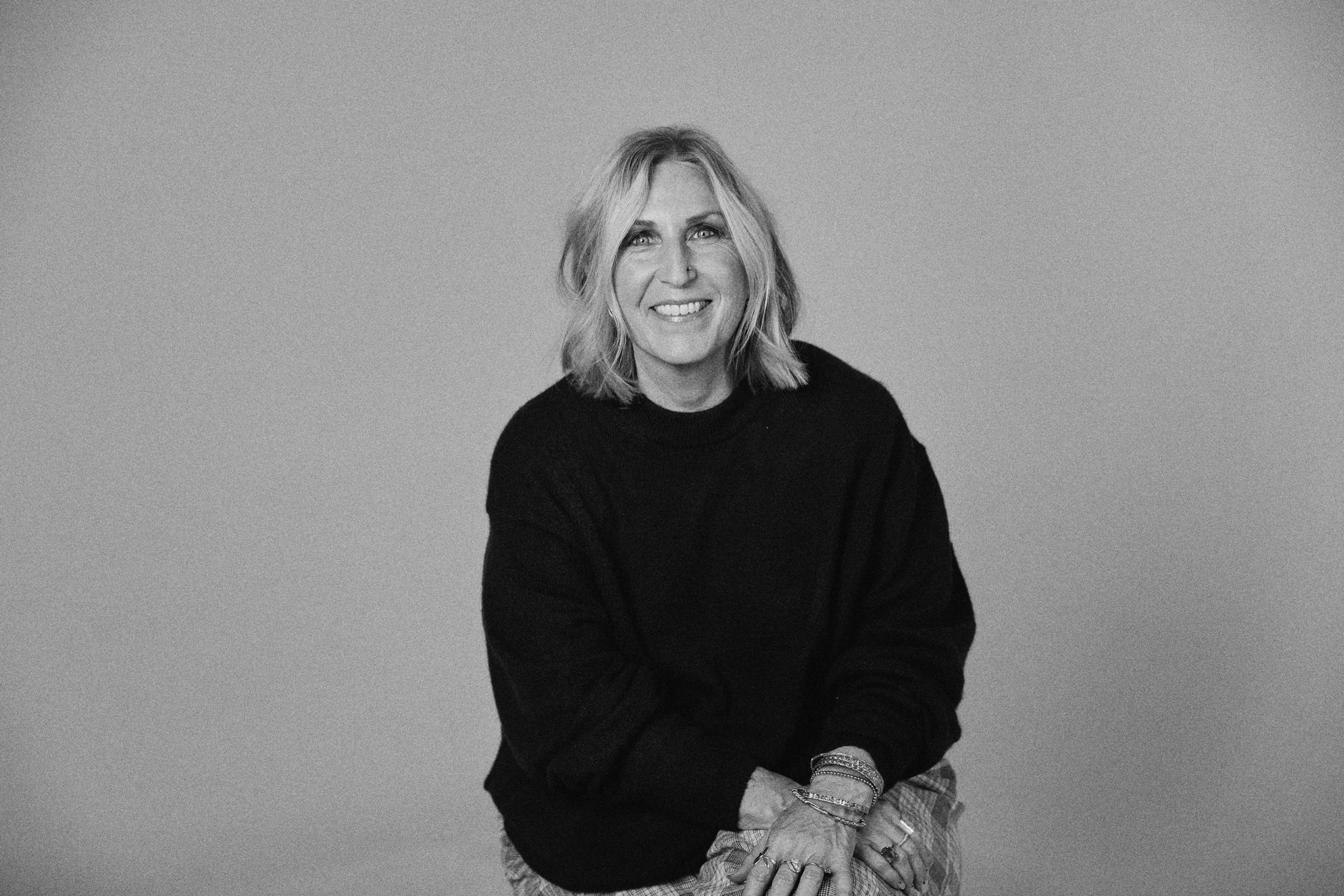 A close-up black-and-white portrait of a woman with wavy blonde hair and expressive eyes, looking directly at the camera.