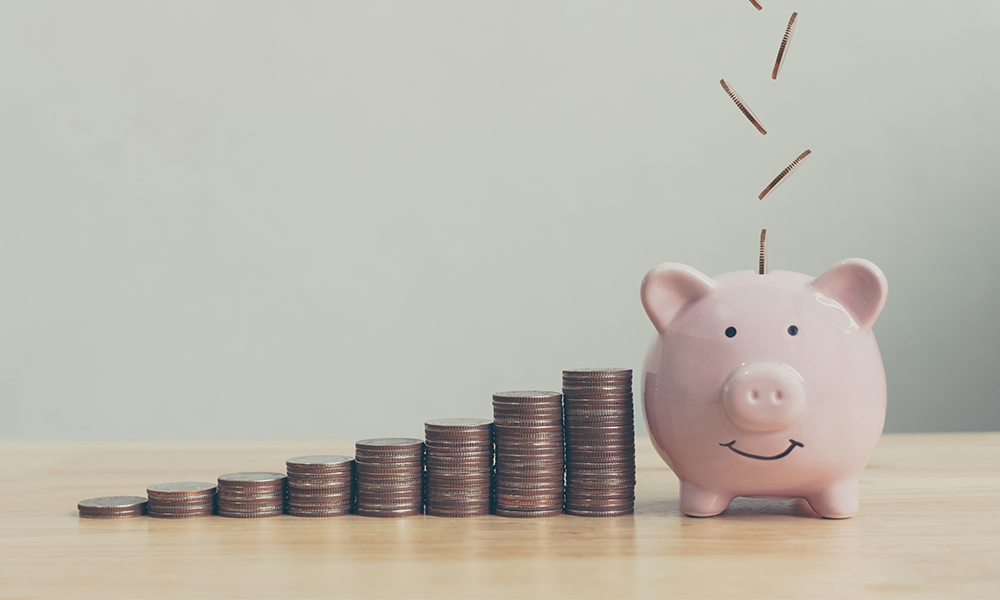 Stacks of quarters sit in gradually increasing sizes. A piggy bank sits next to the tallest stack with quarters raining down into the piggybank slot.