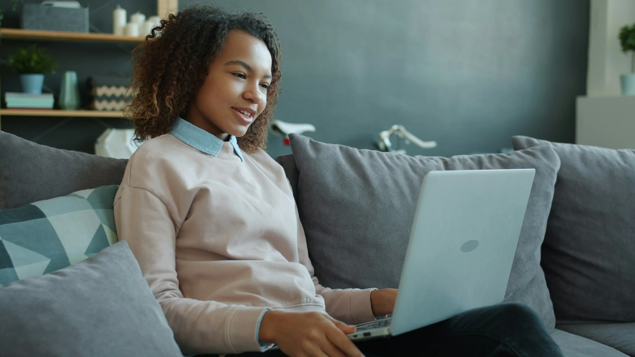 A teen girl with curly hair engaging in therapy online through a laptop.