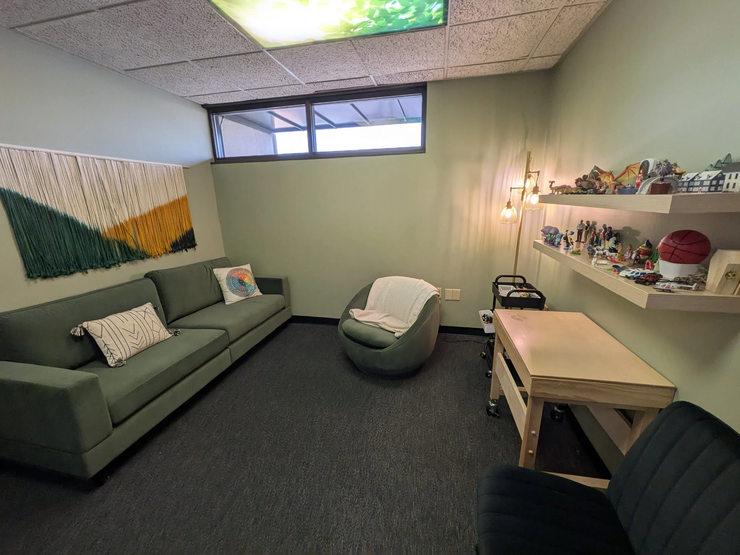 A therapy room with a green couch and green chair with sand tray and toys with green wallls
