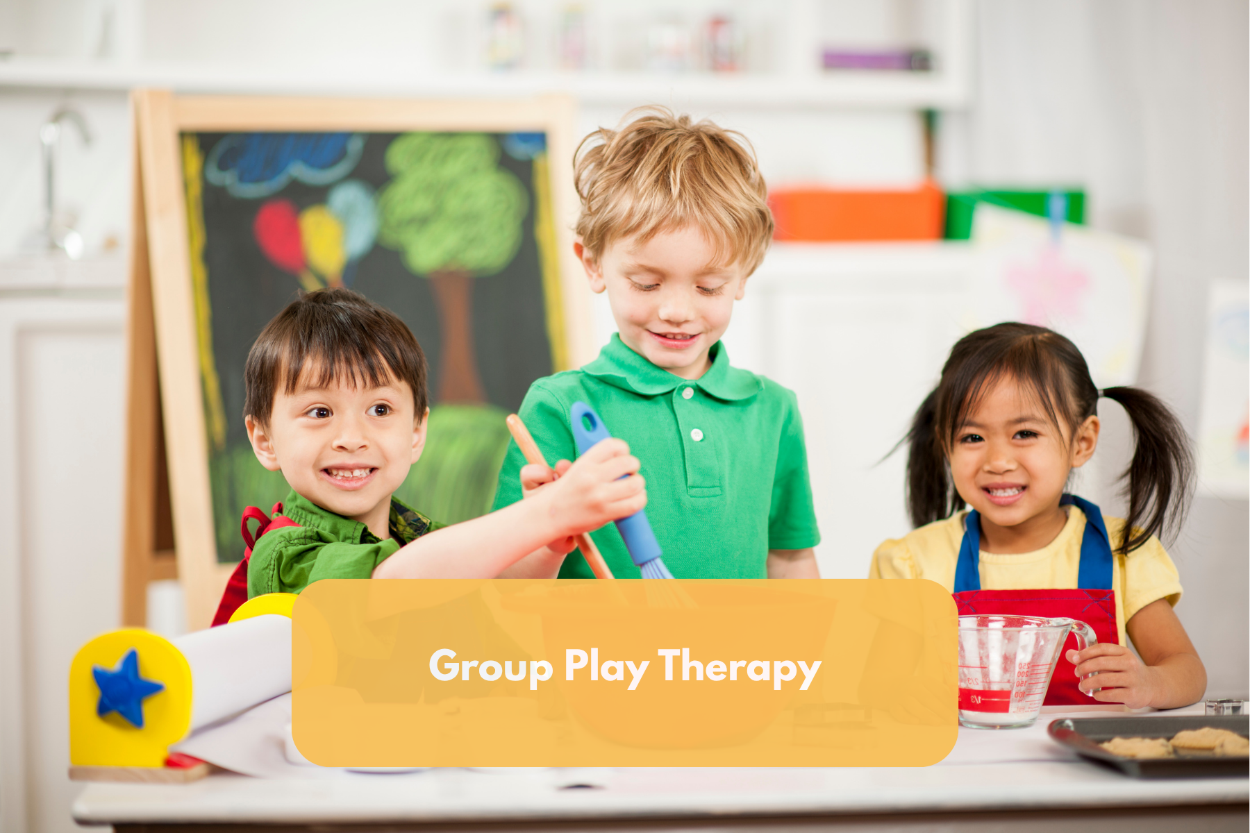 Three children participating in group play therapy, standing at a table with baking utensils and ingredients, with a colorful chalkboard in the background.