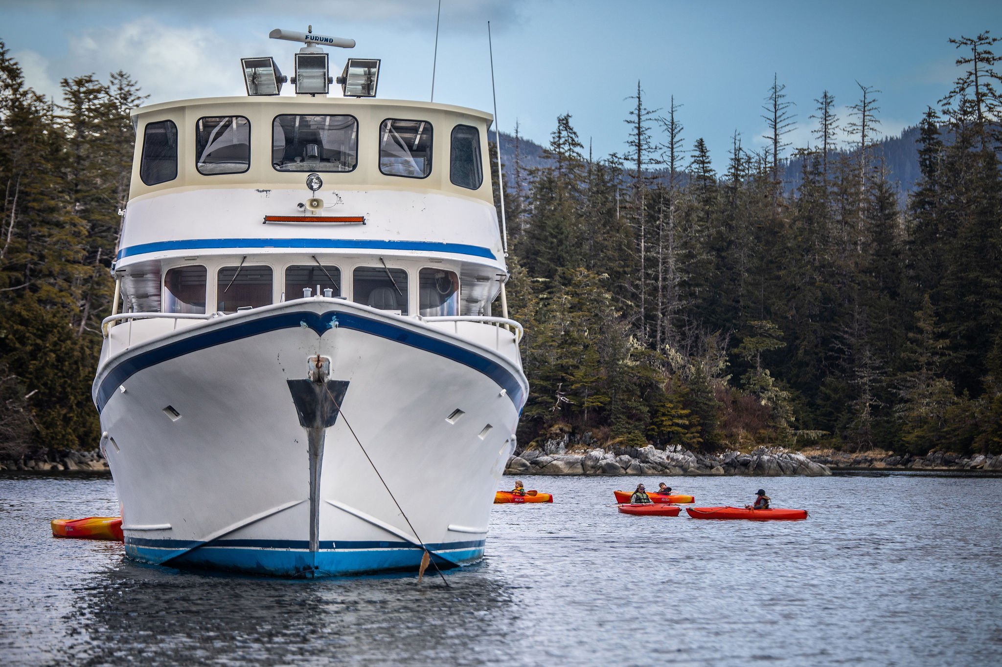 Head on view of the Silver Lady at anchor in a cove while kayakers depart from her stern.