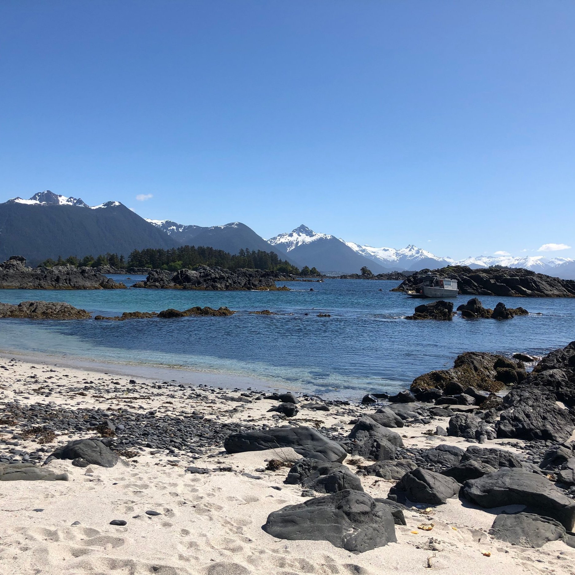 White sandy beach with volcanic rock, mountains in the distance and blue water.