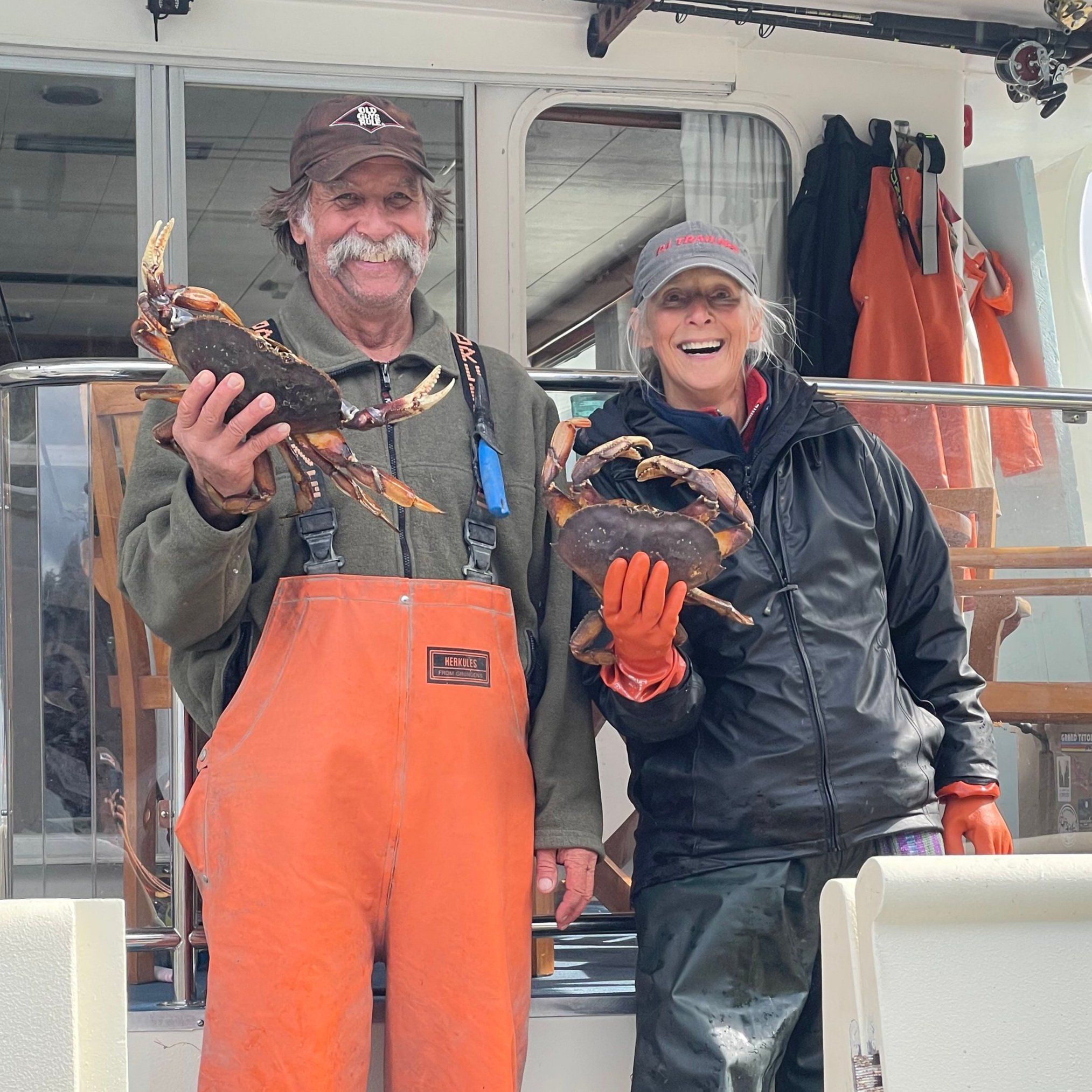 A couple shows off two Dungeness crab standing ont he stern of the Silver Lady in rain gear and baseball hats.
