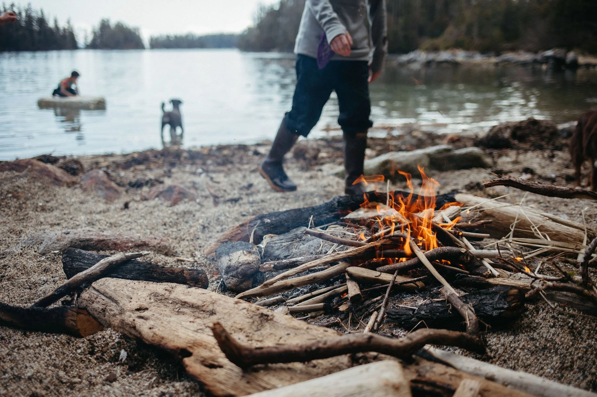 Fire-on-beach-person-approaching-and-dog-and-kayaker-at-water-edge-blurred-in-background.jpg