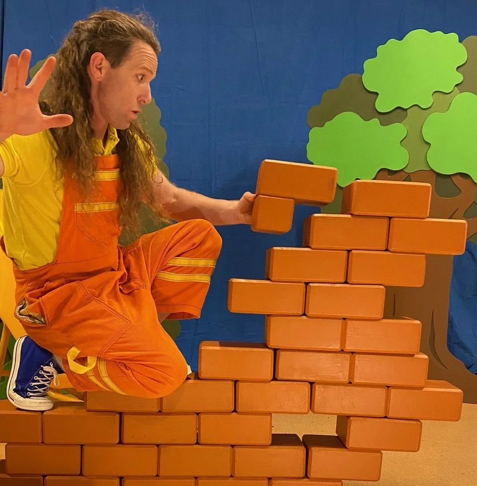 An actor balances on a brick wall as he adds bricks to it.