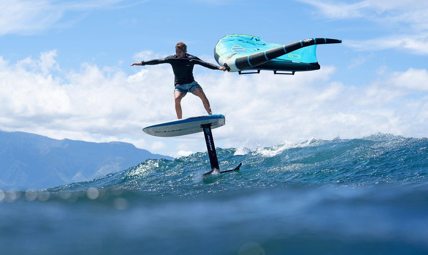 Wing foiler riding a wave with a turquoise Naish wing