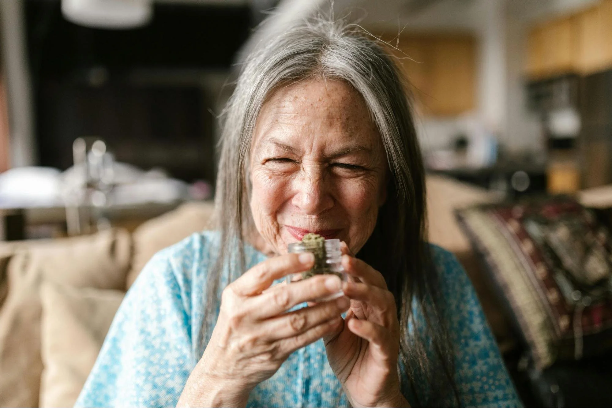 An elderly woman smelling cannabis in a jar. Source - Pexels