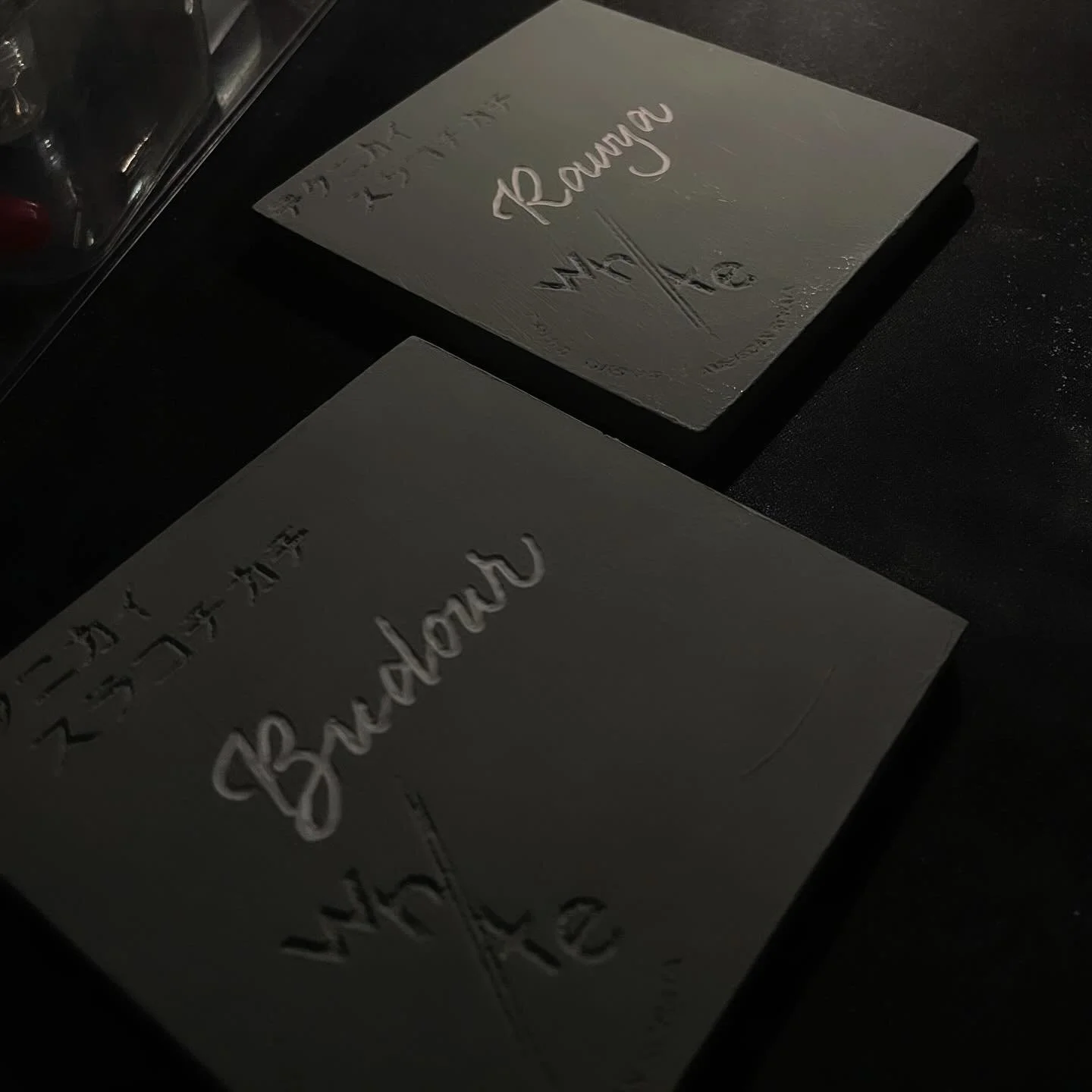 Two white cards with embossed words, one reads 'Rainbow', and the other has partially visible text, on a dark surface.