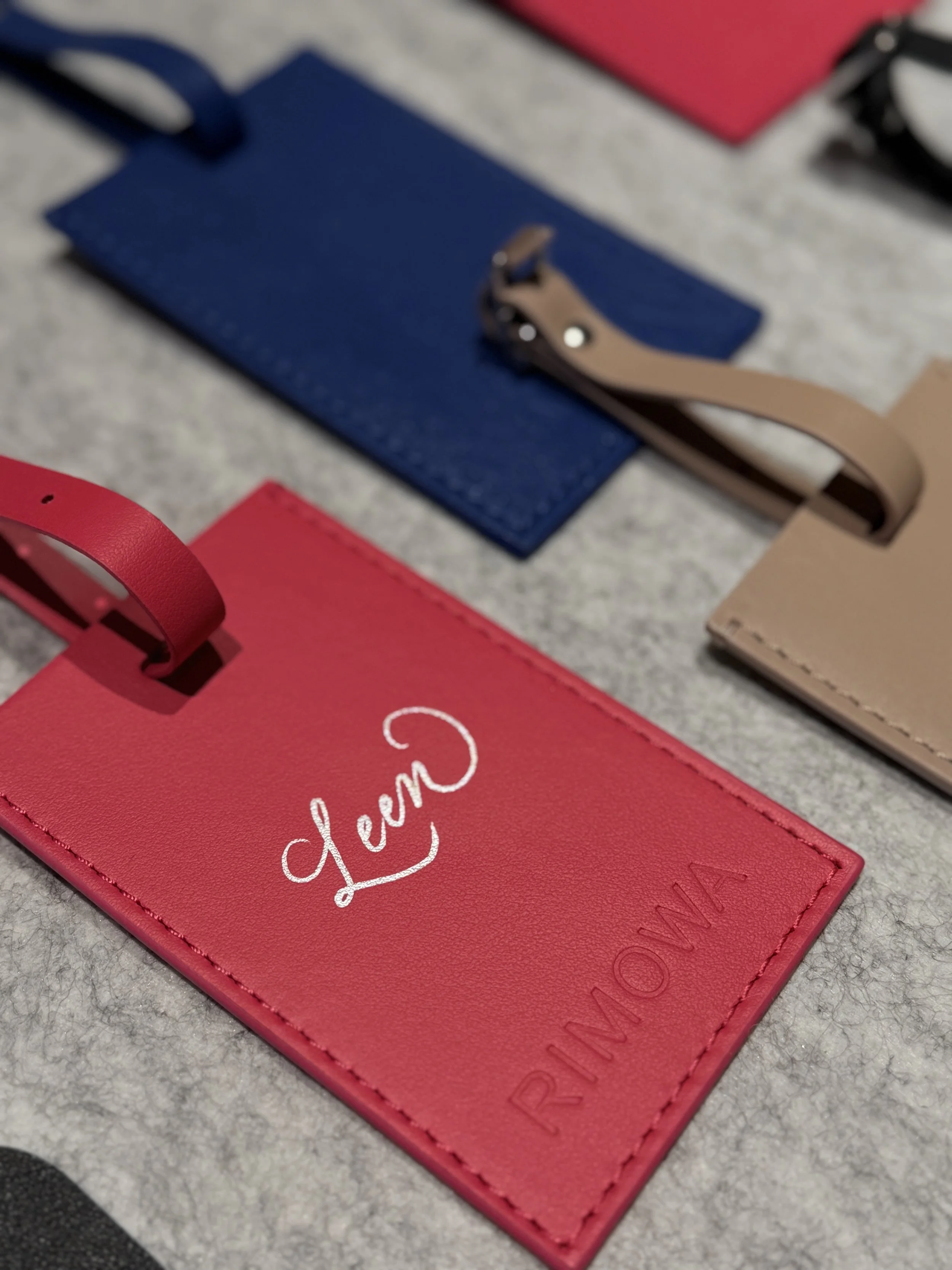 Close-up of red, blue, and beige leather tags with cursive and embossed text, placed on a gray textured surface.