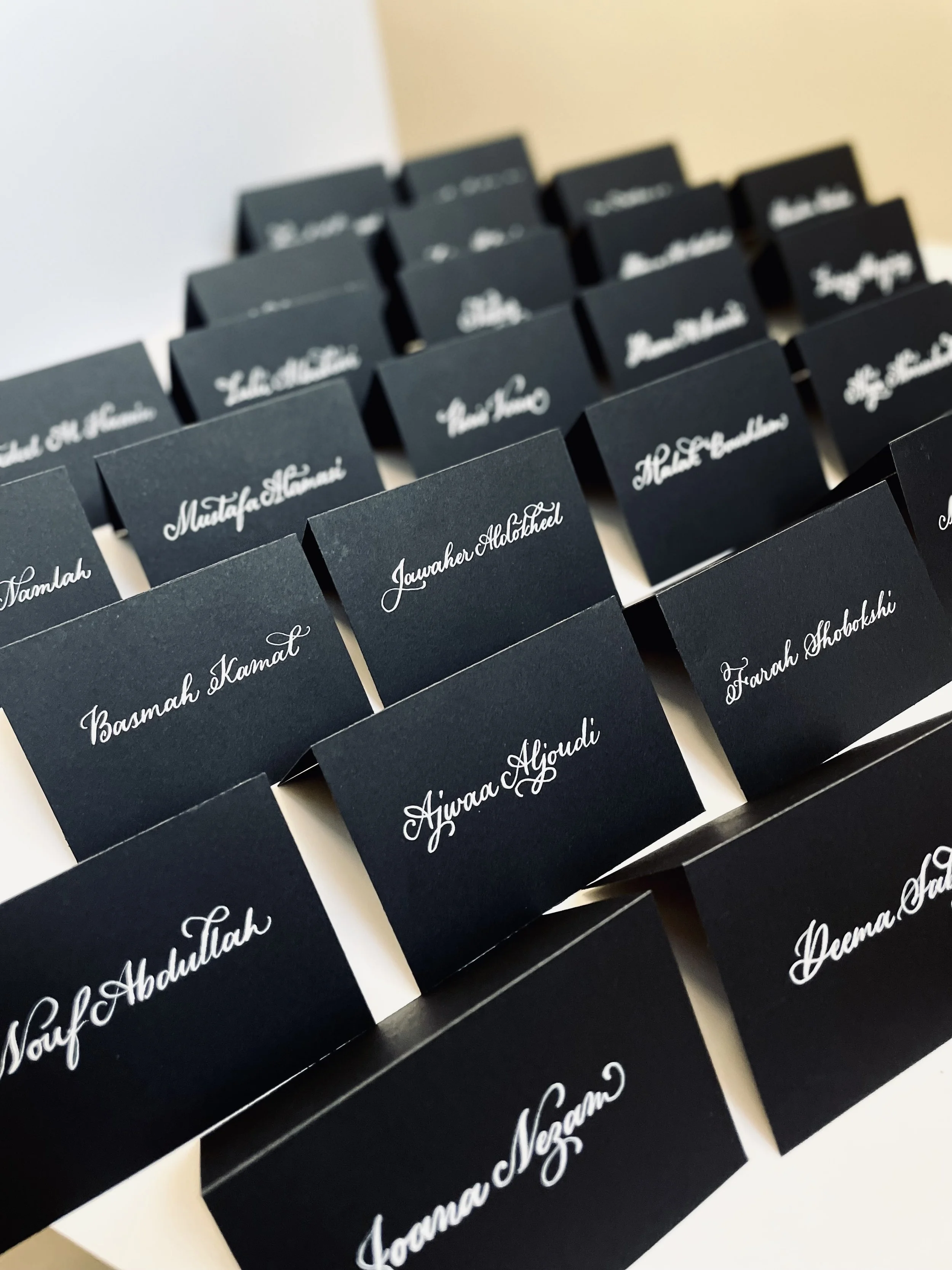 Black name tags with white cursive text, arranged in rows on a white surface.