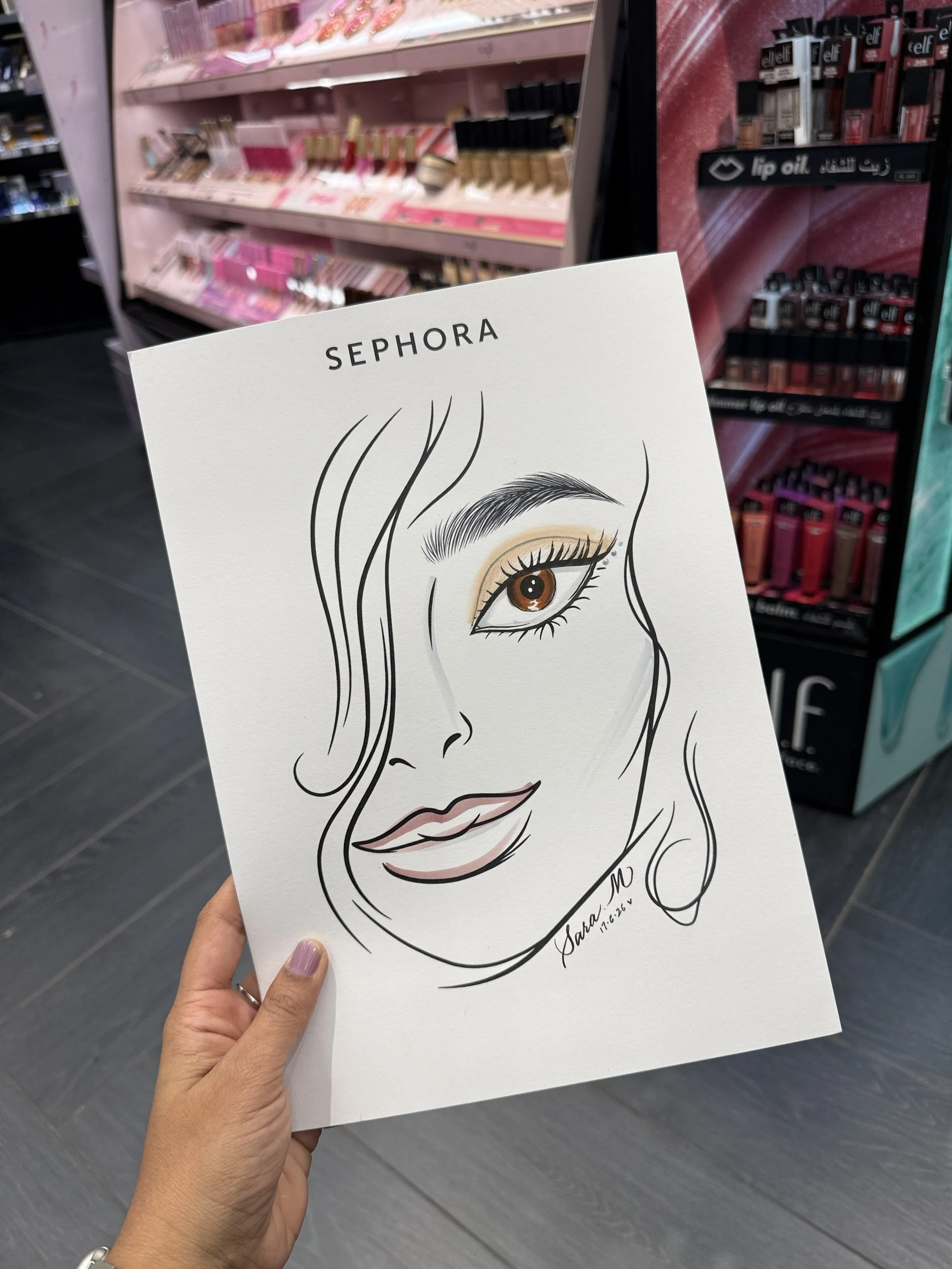 Drawing of a woman's face with detailed eye, eyebrow, and lips, with long wavy hair, labeled 'Sephora' at the top, held in a person's hand in a store aisle.