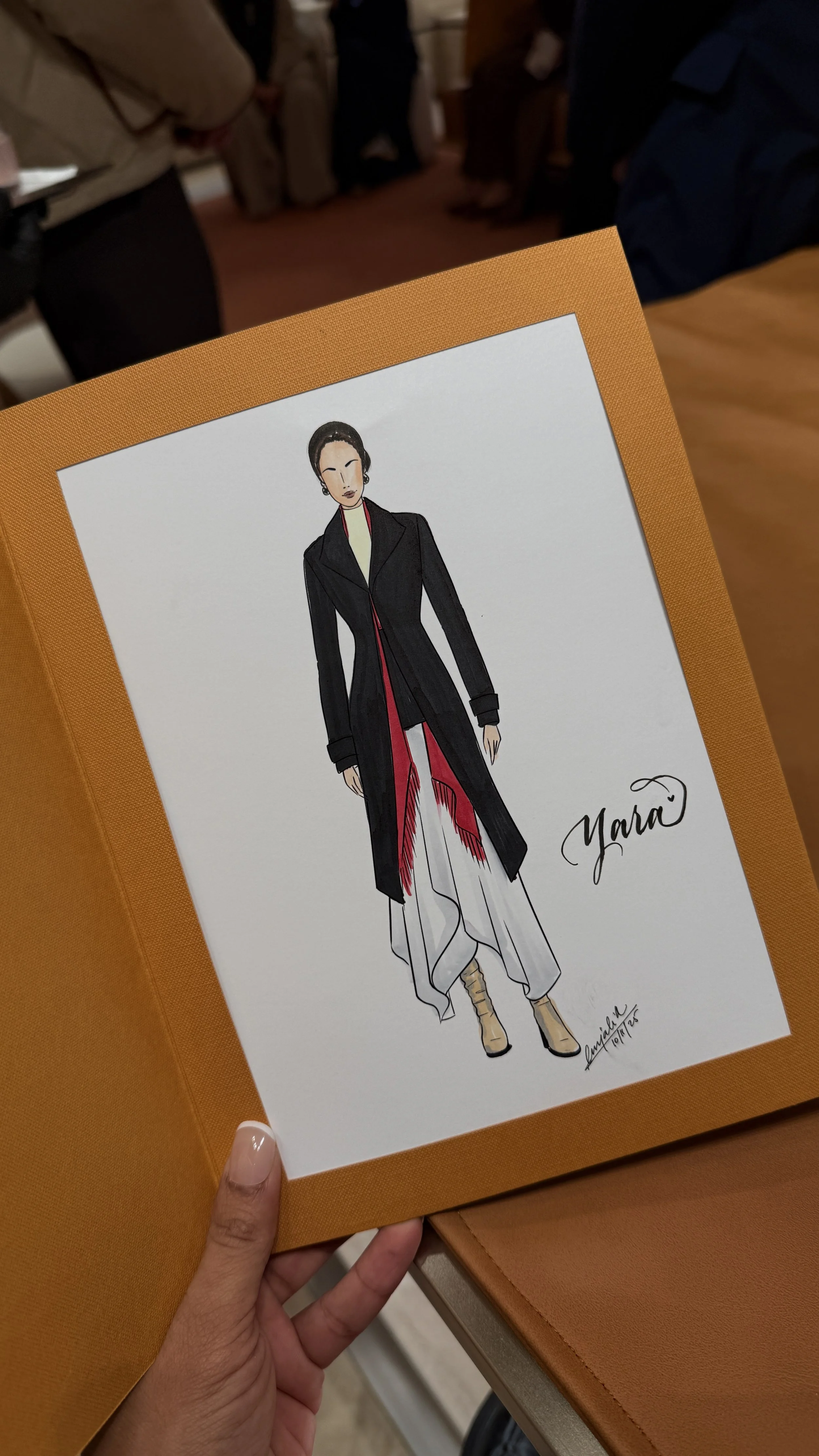 Fashion illustration of a woman wearing a long black coat over a white and red outfit, with beige high-heeled shoes, signed 'Yara'.