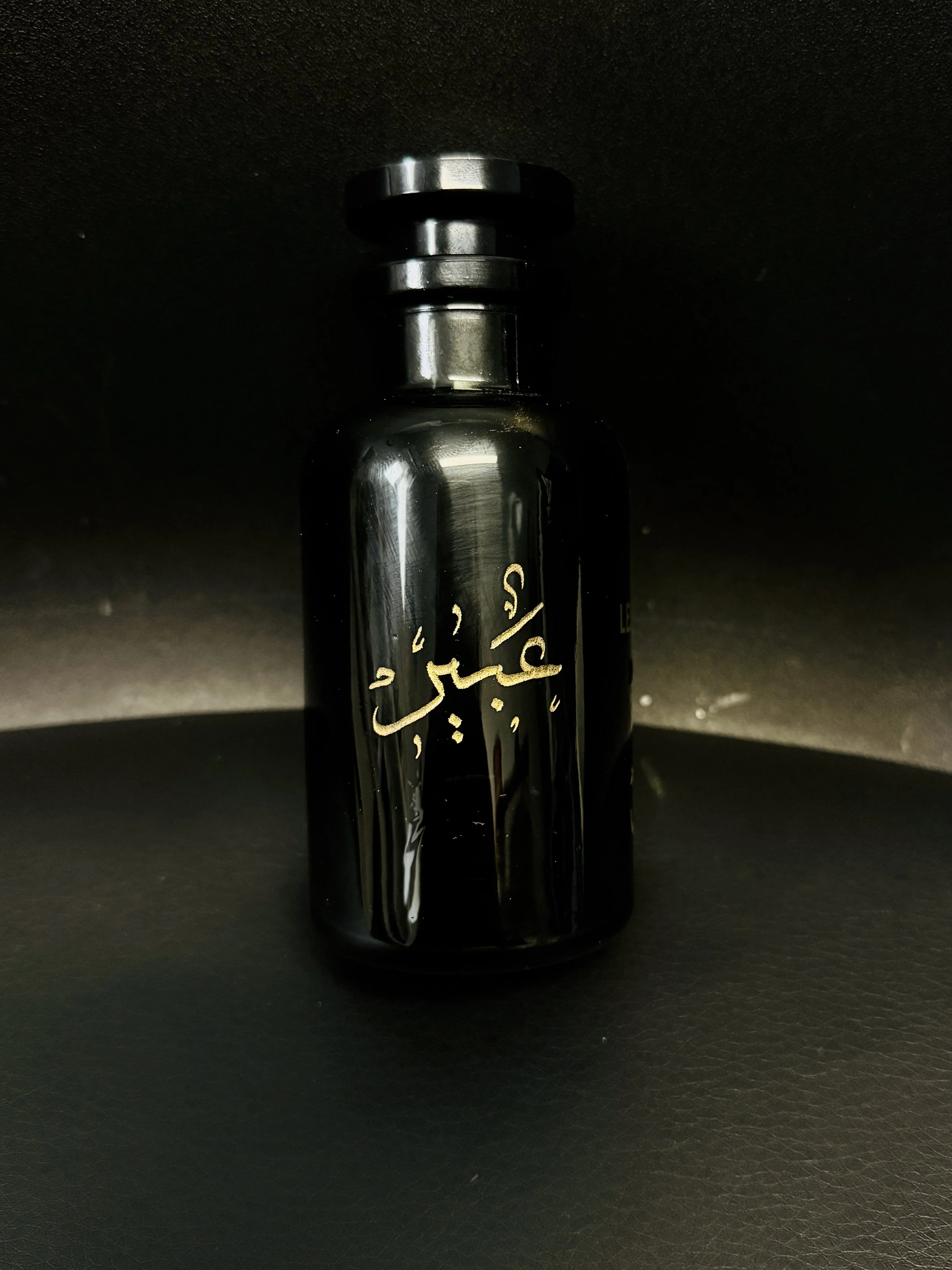 A black bottle with gold script on it sitting on a black surface in a dark environment.
