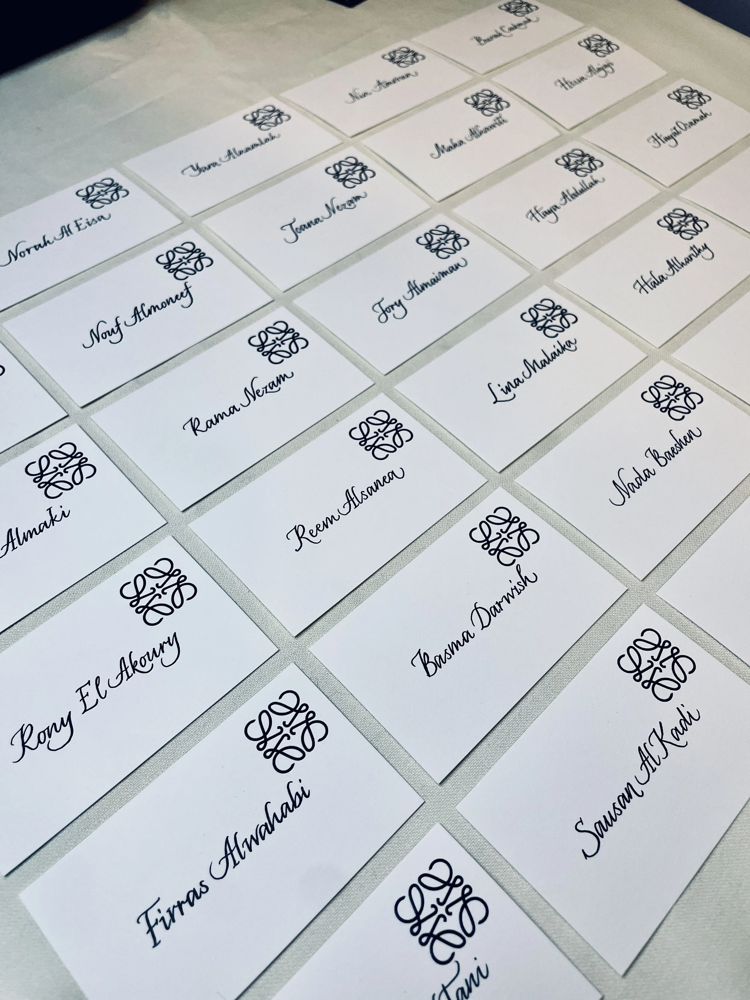 A sheet of white name cards with black cursive writing and a decorative logo, arranged in rows on a table.