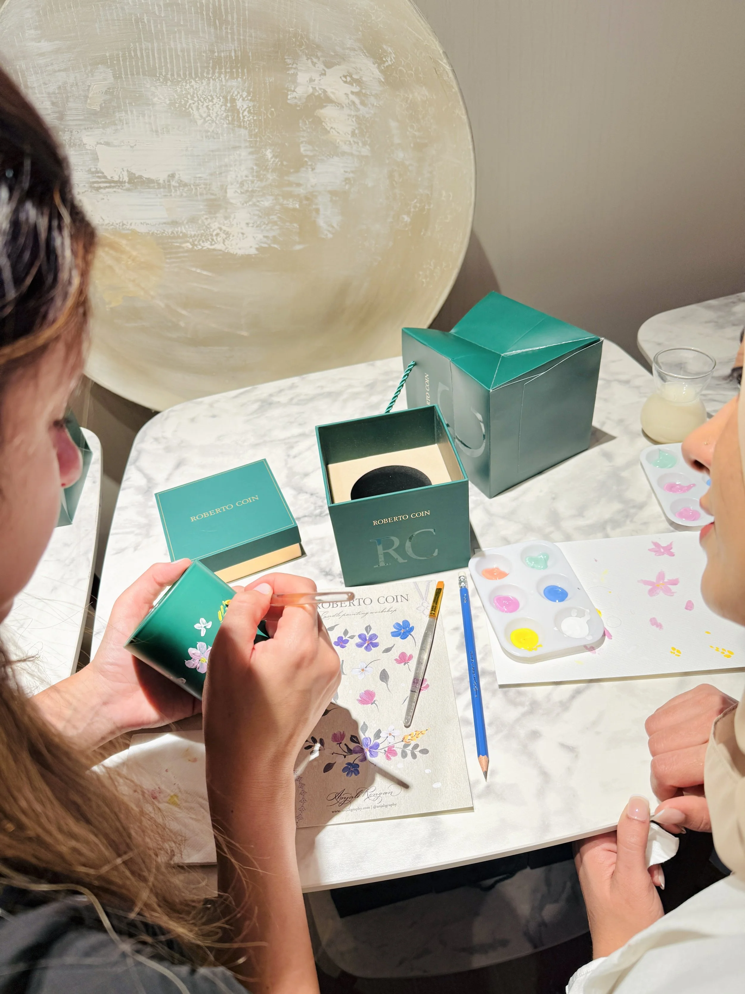 People painting floral designs on small cylindrical containers during an arts and crafts activity at a table.