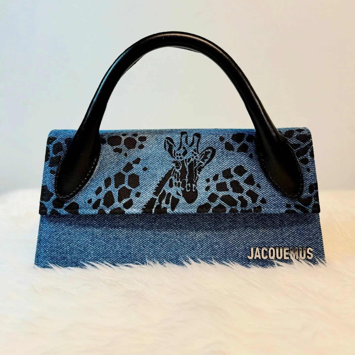 Jacquemus handbag with denim fabric, black leopard print giraffe face design, black leather handles, and metallic logo.