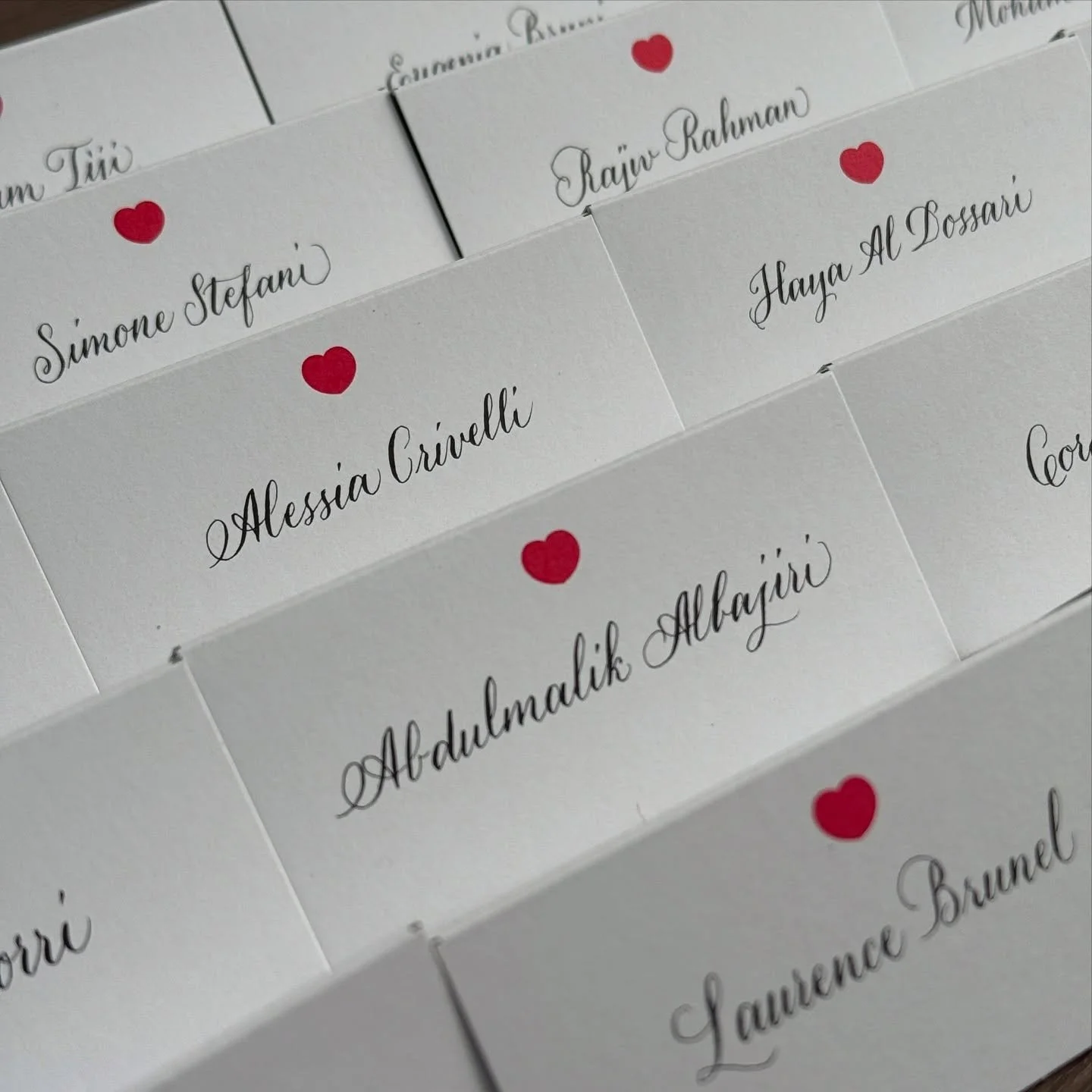 Name tags with red heart icons and elegant black cursive font, including names such as Simone Stefani, Alessia Crivelli, Raju Rahman, Haya Al Bossari, and Abdulkadir Albayir.