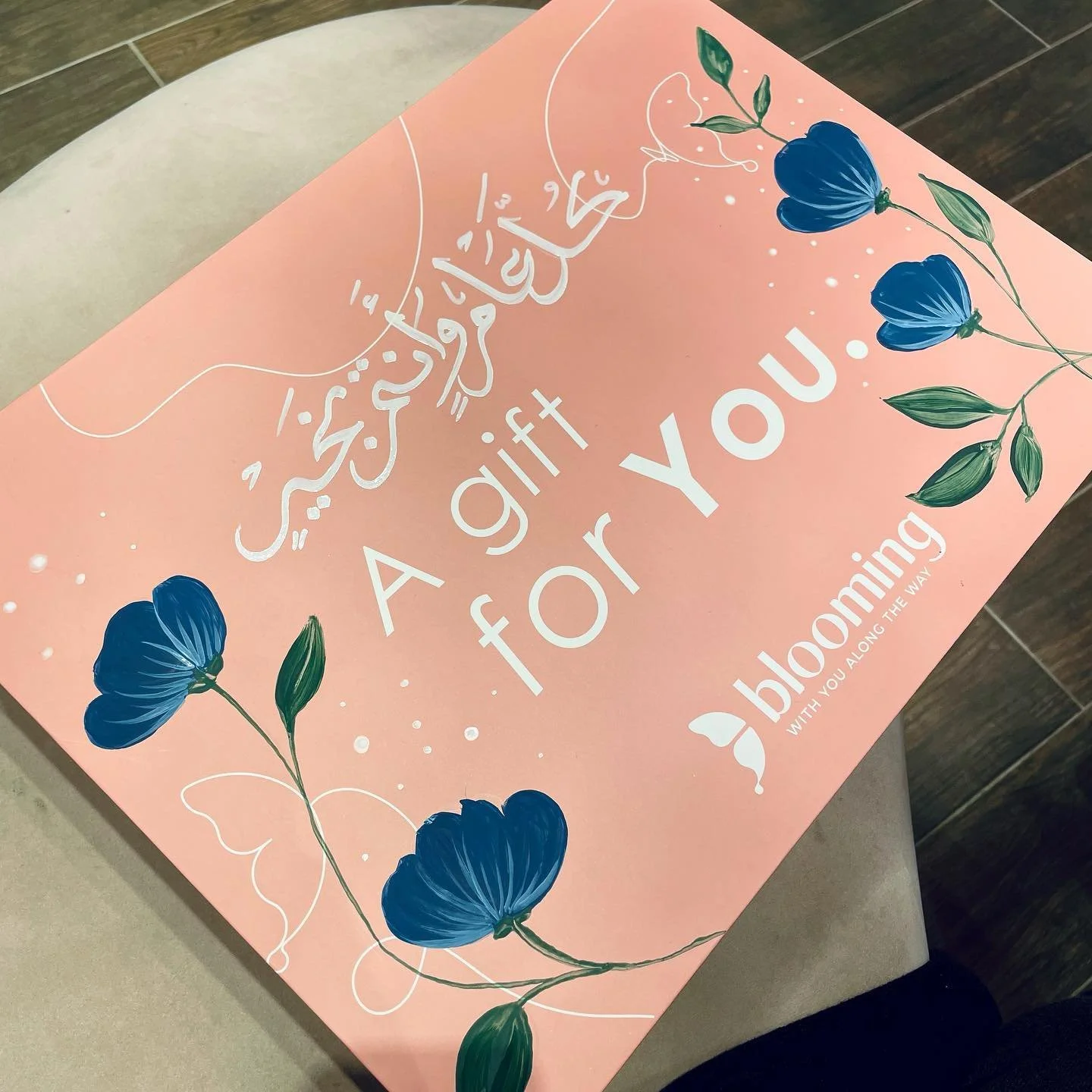 A pink card with white and dark blue floral illustrations. White text reads 'A gift for you.' The bottom right corner has smaller text saying 'with you along the way.'