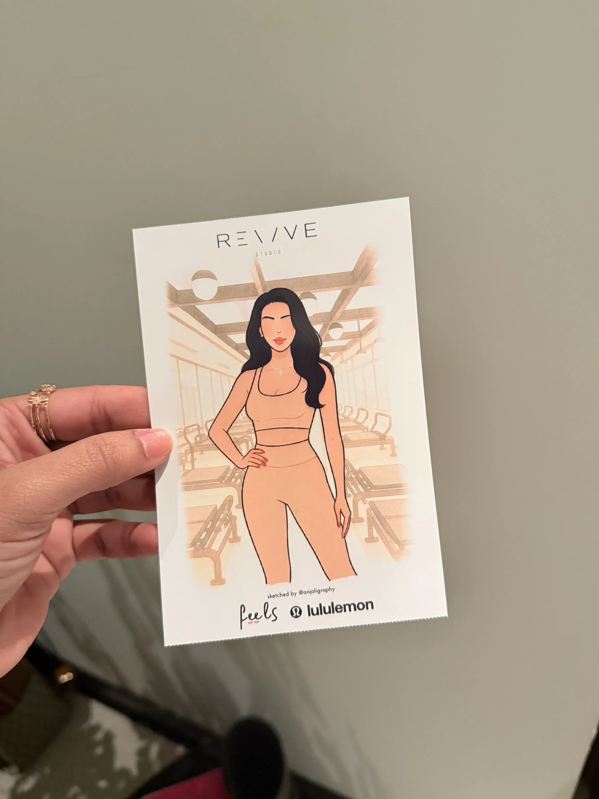 A hand holding a flyer with an illustration of a woman in workout clothes, standing with one hand on her hip, in a gym setting with chairs and gym equipment in the background.