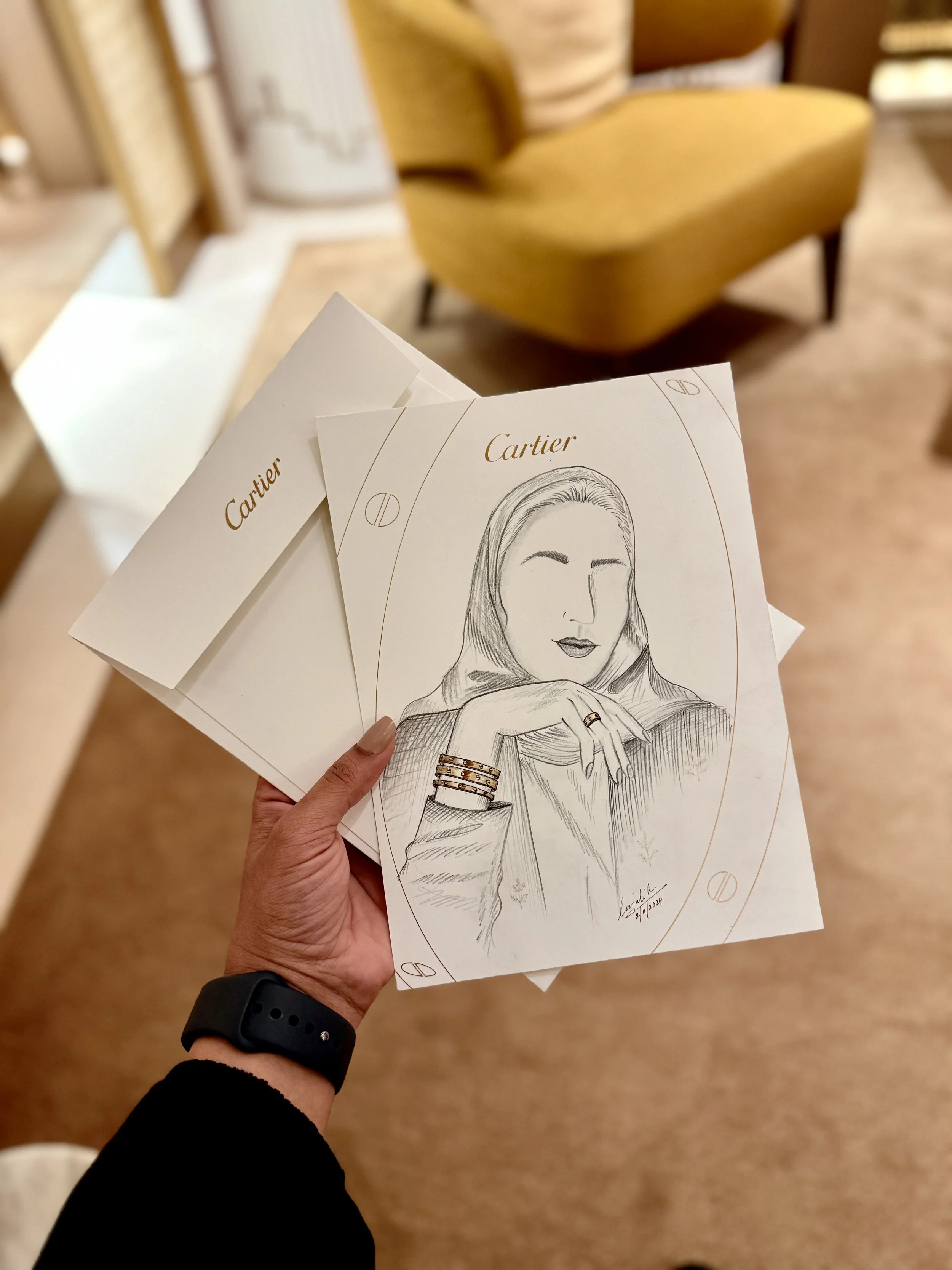 Person holding sketch of a woman with jewelry, with a yellow chair in the background.