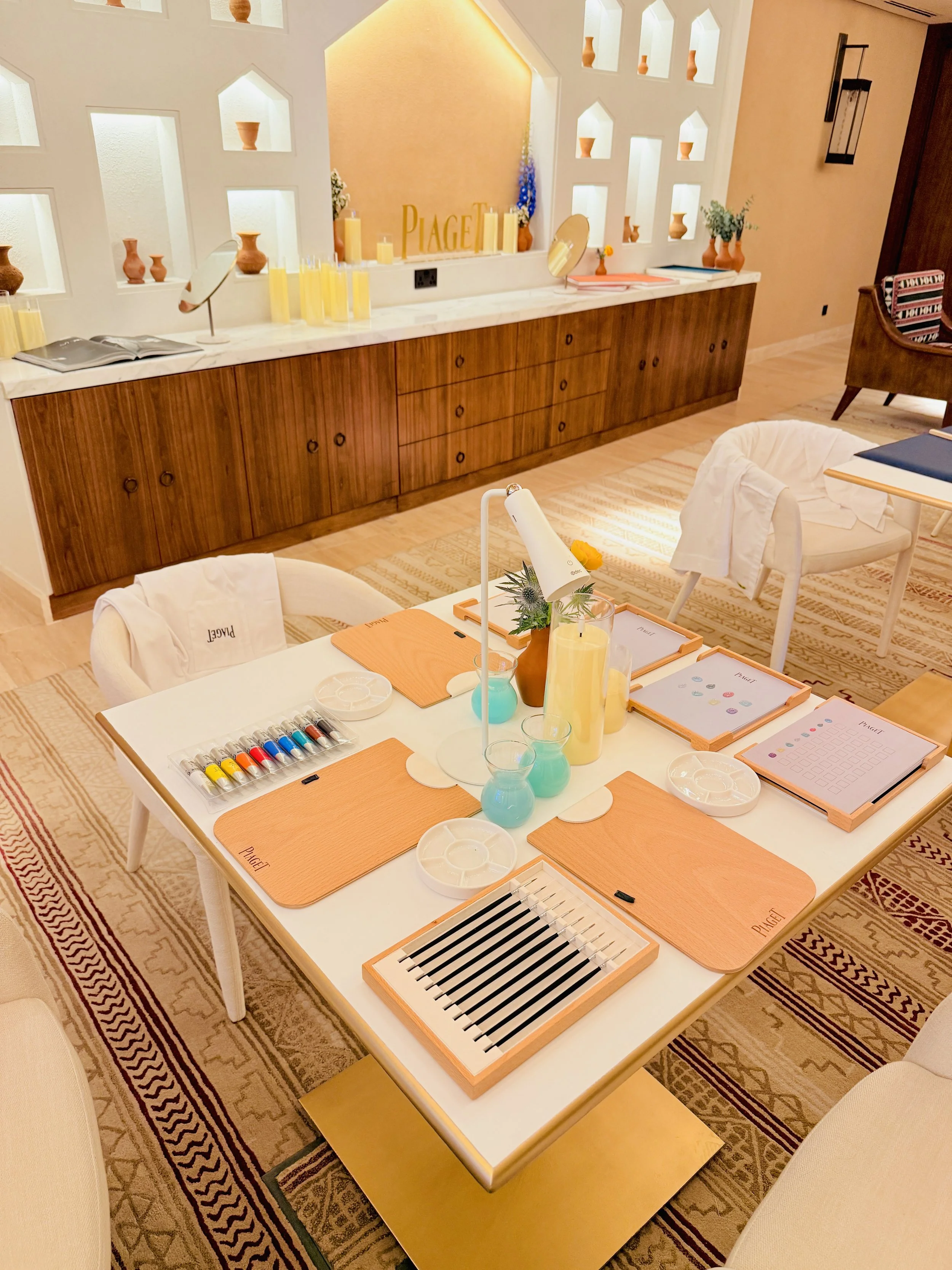 A table set up for a paint and sip activity with paintbrushes, palettes, and alcohol inks, along with floral decorations and pink 