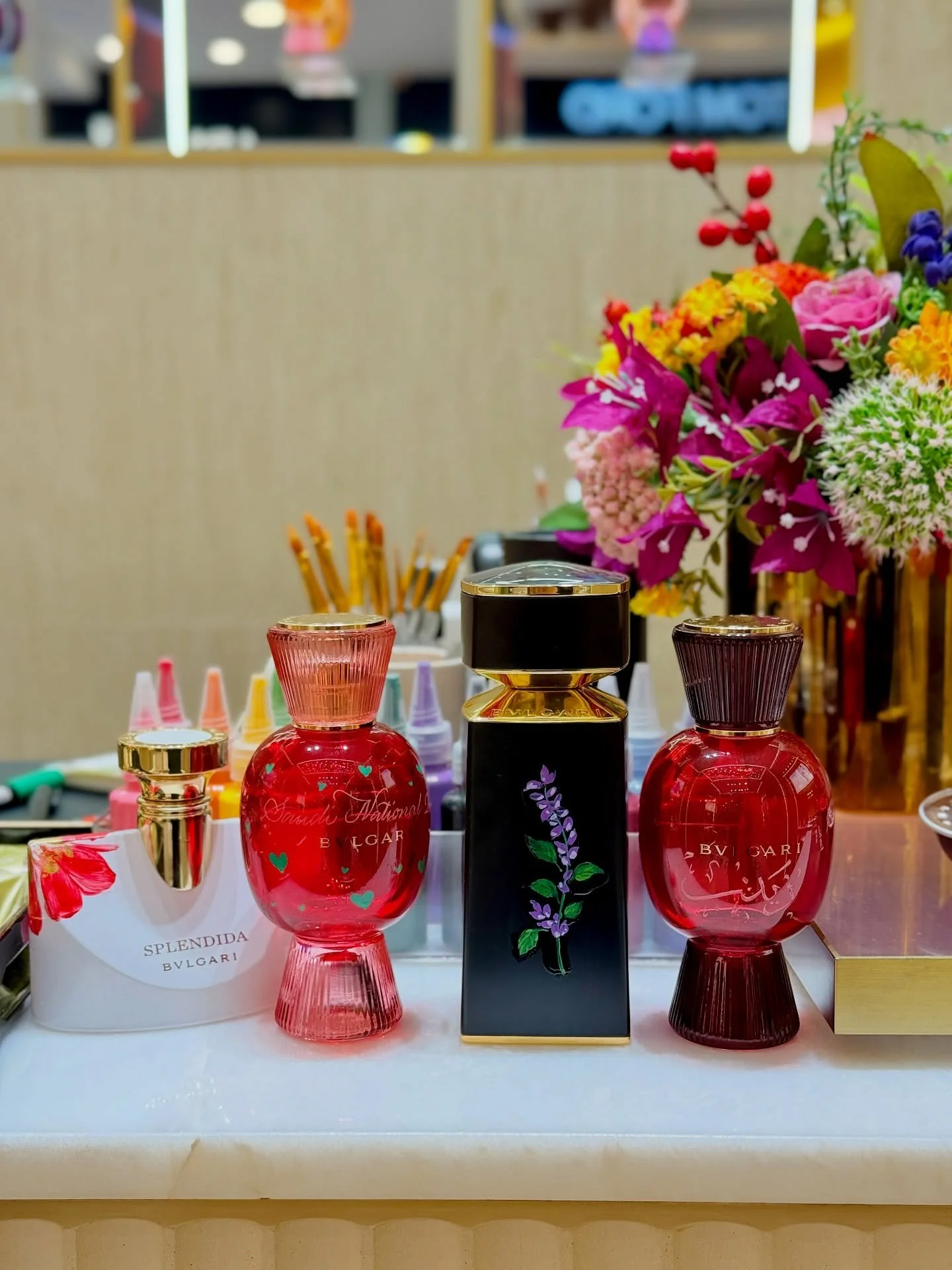 A display of perfume bottles on a table with a bouquet of colorful flowers in the background.