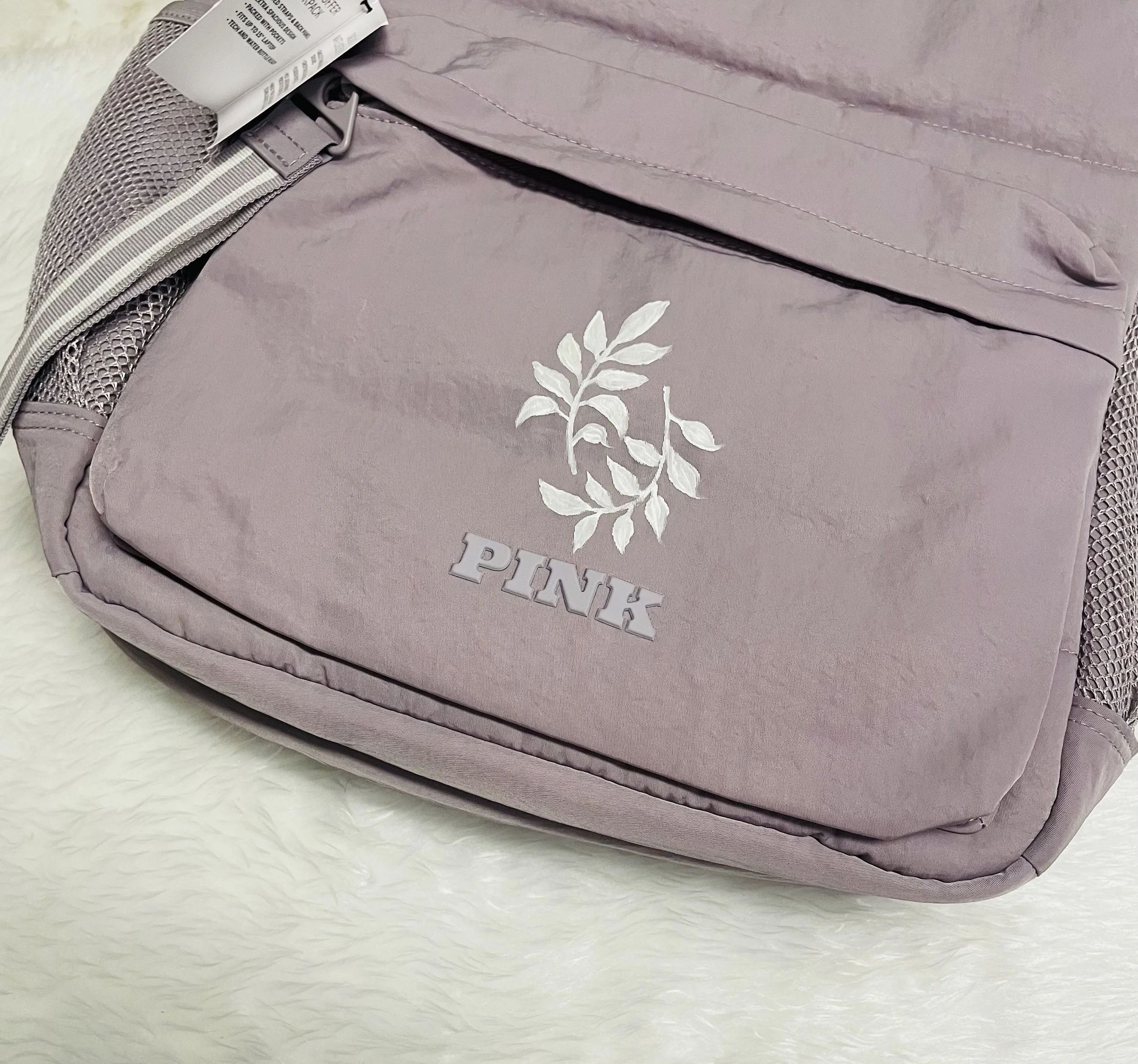A close-up of a purple item, possibly a handbag or backpack, with a zipper and floral design, resting on a white fuzzy surface.