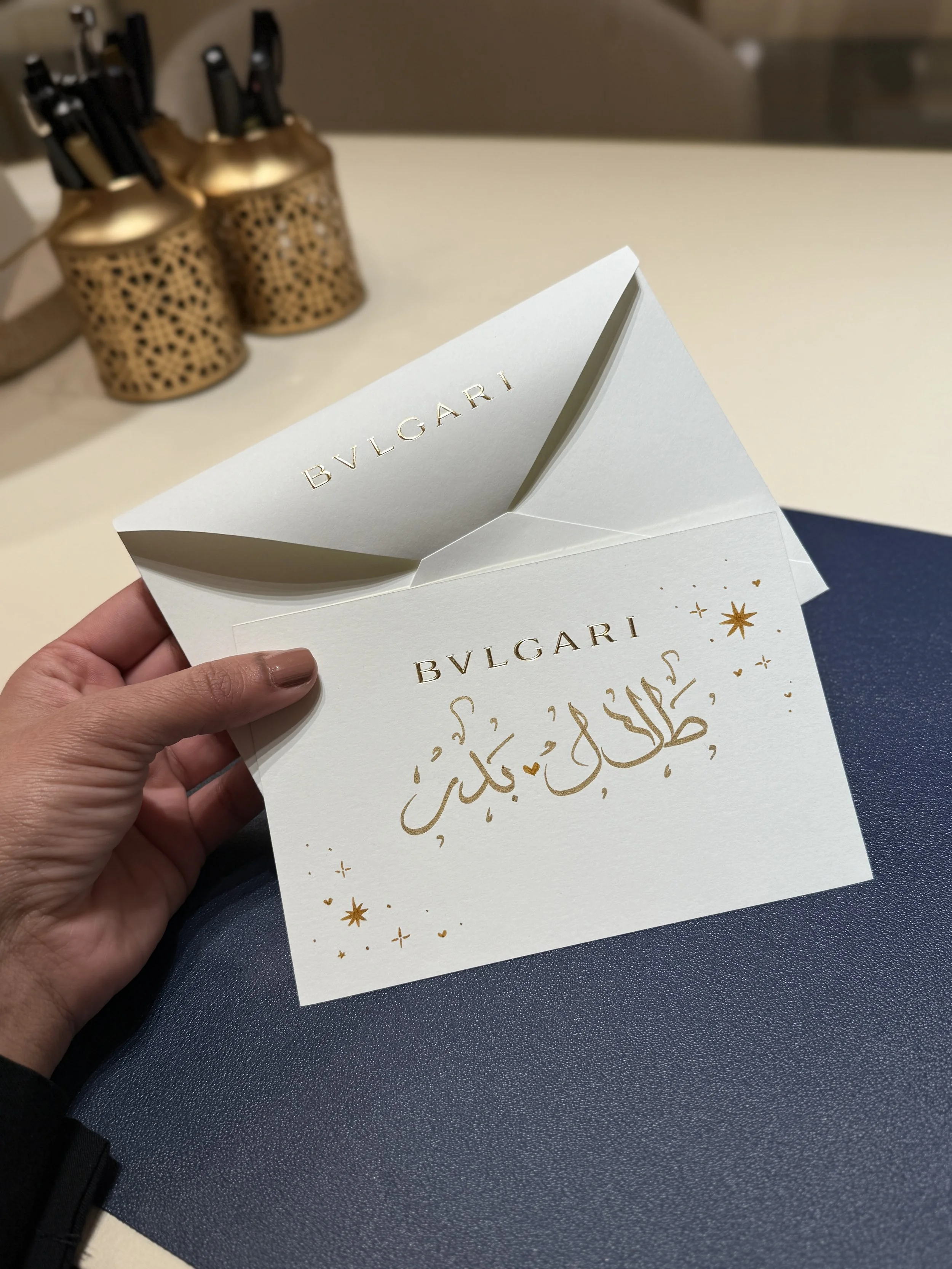 Luxury holiday card with gold lettering and holiday decorations, held by a person's hand.