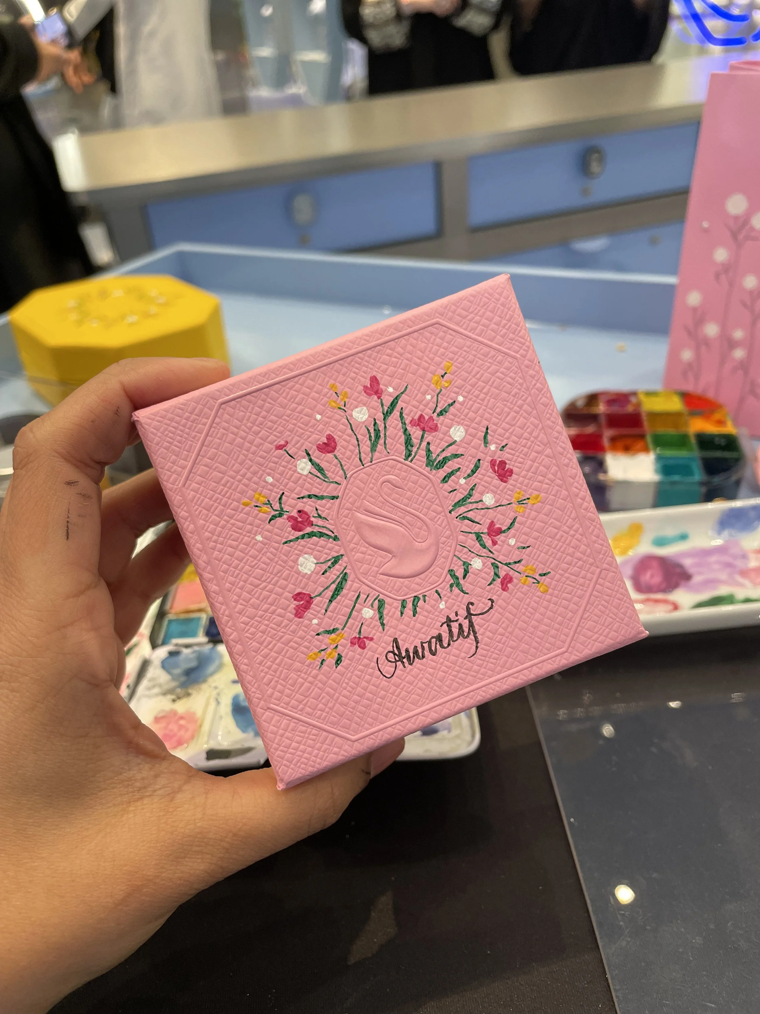A person holding a pink textured card with a decorative floral design and the word "Gratitude" written on it.