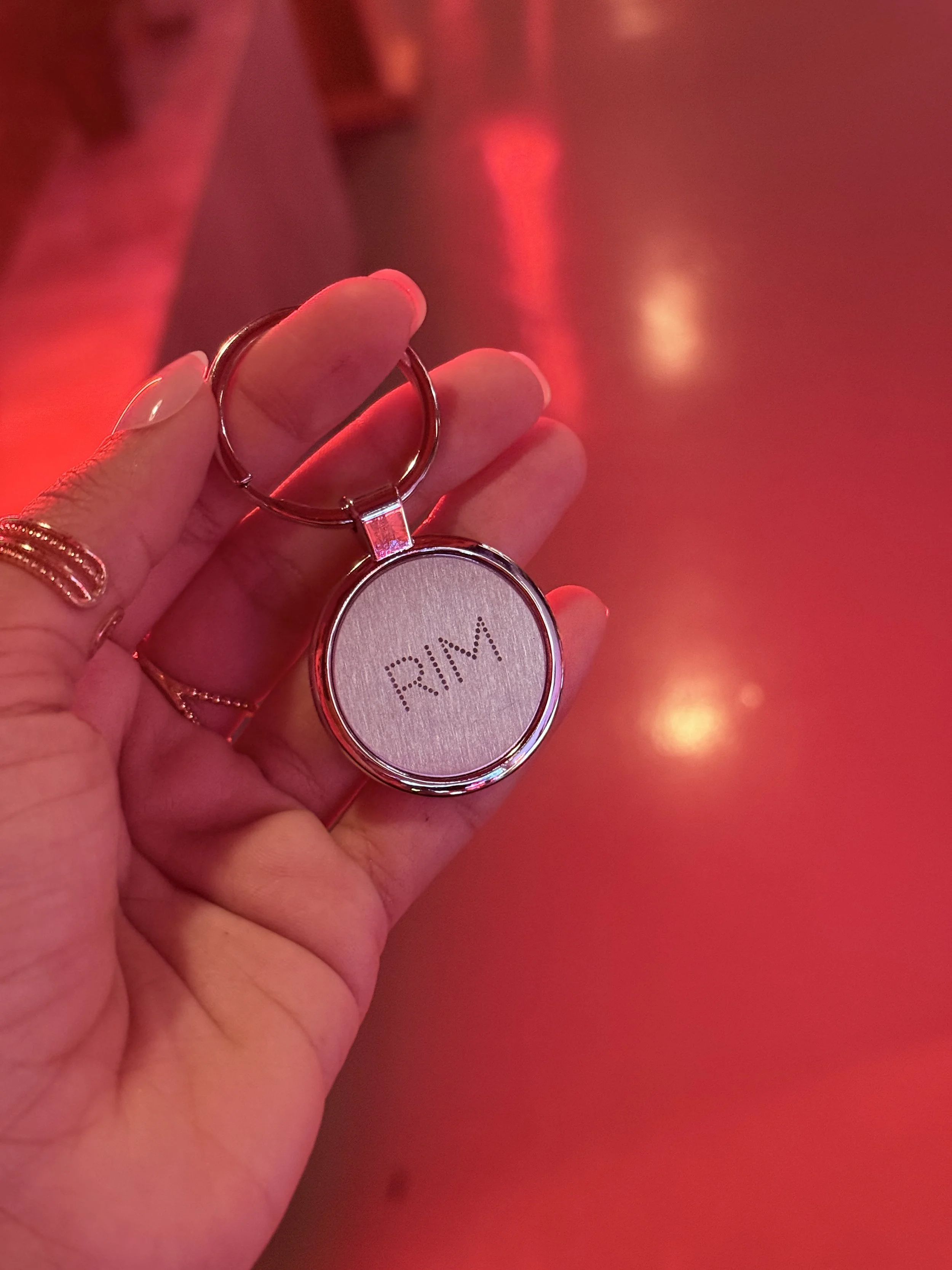 A hand holding a round keychain with the word 'RIM' on it, against a red background with reflections of red lights.